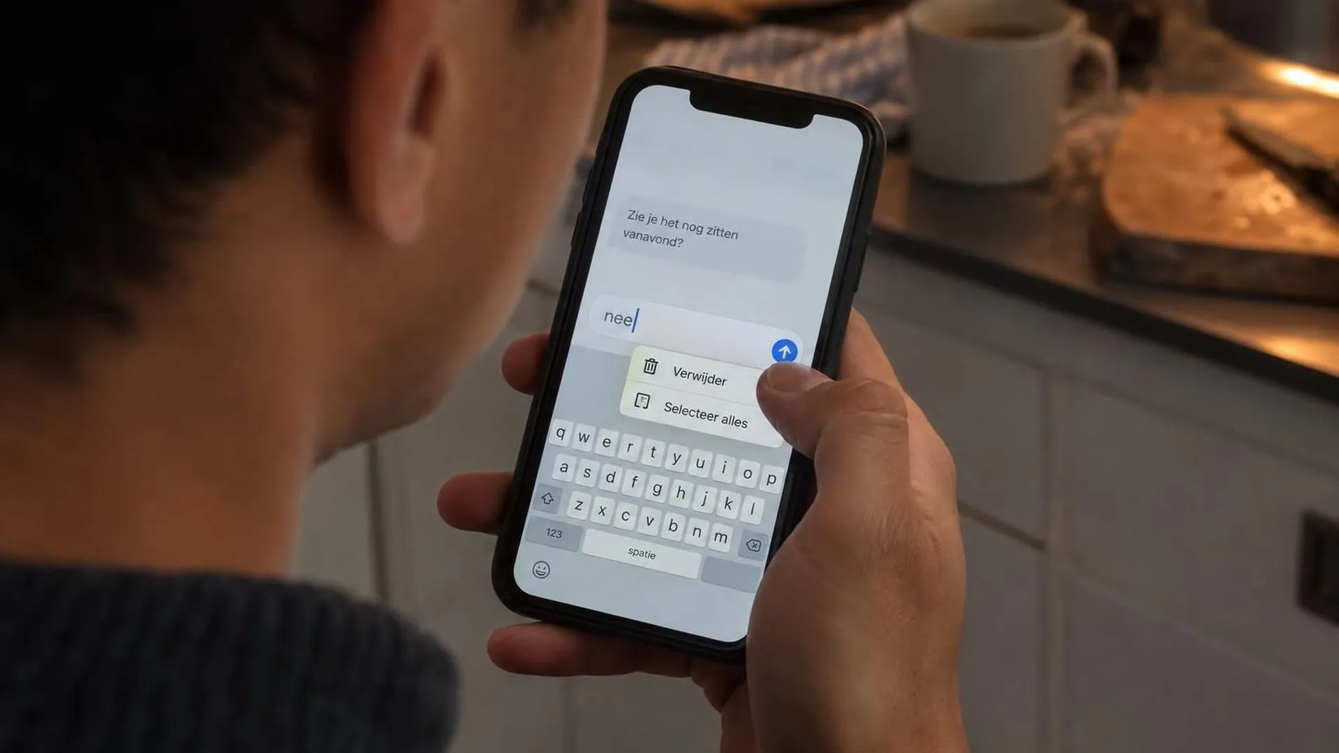 Close-up van een hand die aarzelt boven een net getypt 'nee'-bericht op een telefoon, vlak voordat het gewist wordt.