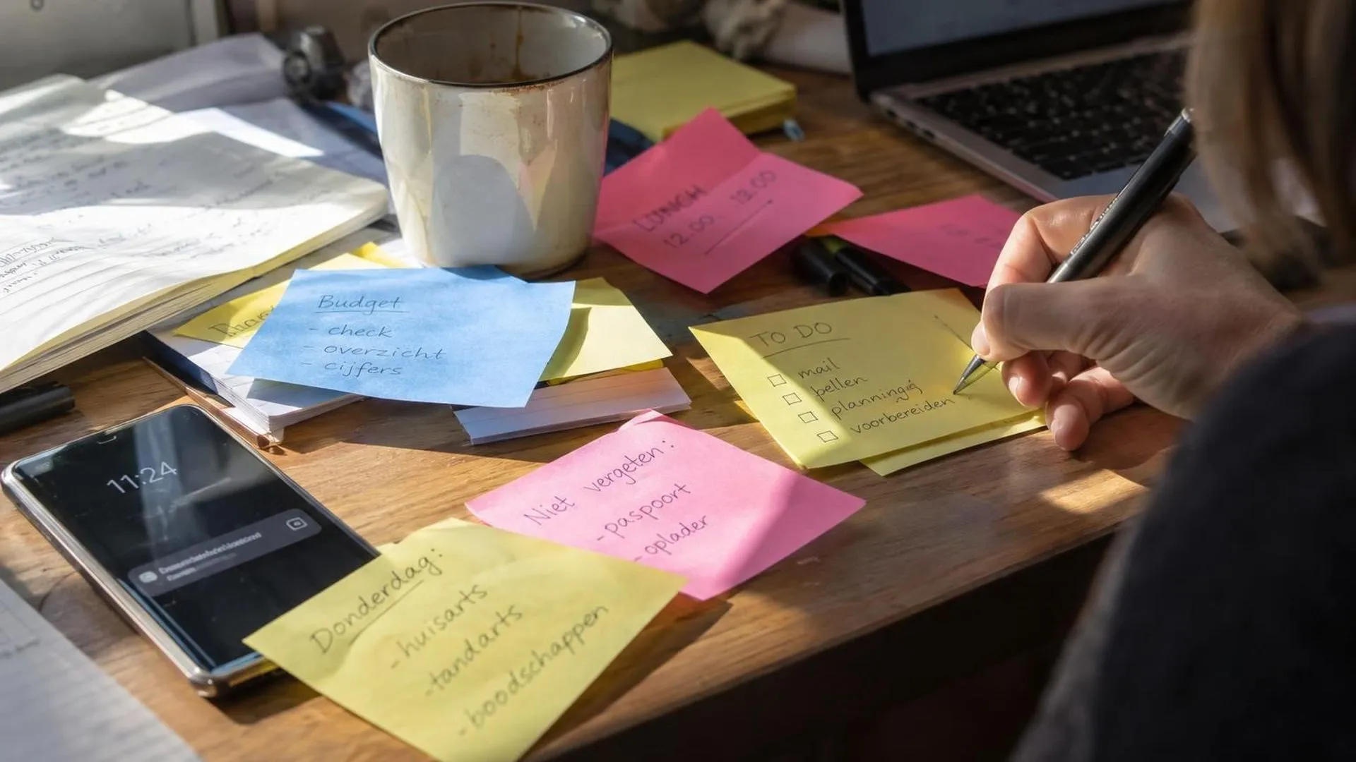 Close-up van een bureau vol overlappende Post-its met een trillende telefoon aan de rand van beeld.