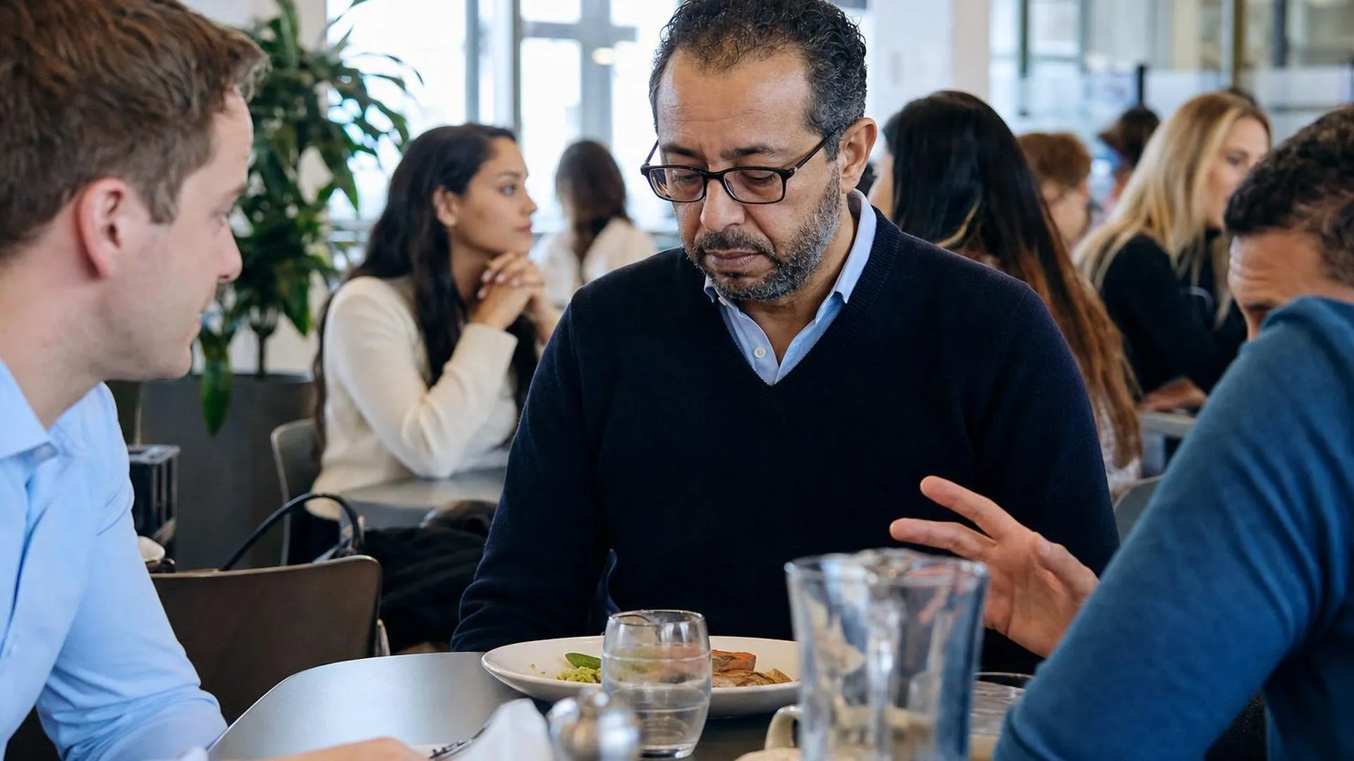Persoon zit stil aan een drukke lunchkamer tafel, ogenschijnlijk afwezig