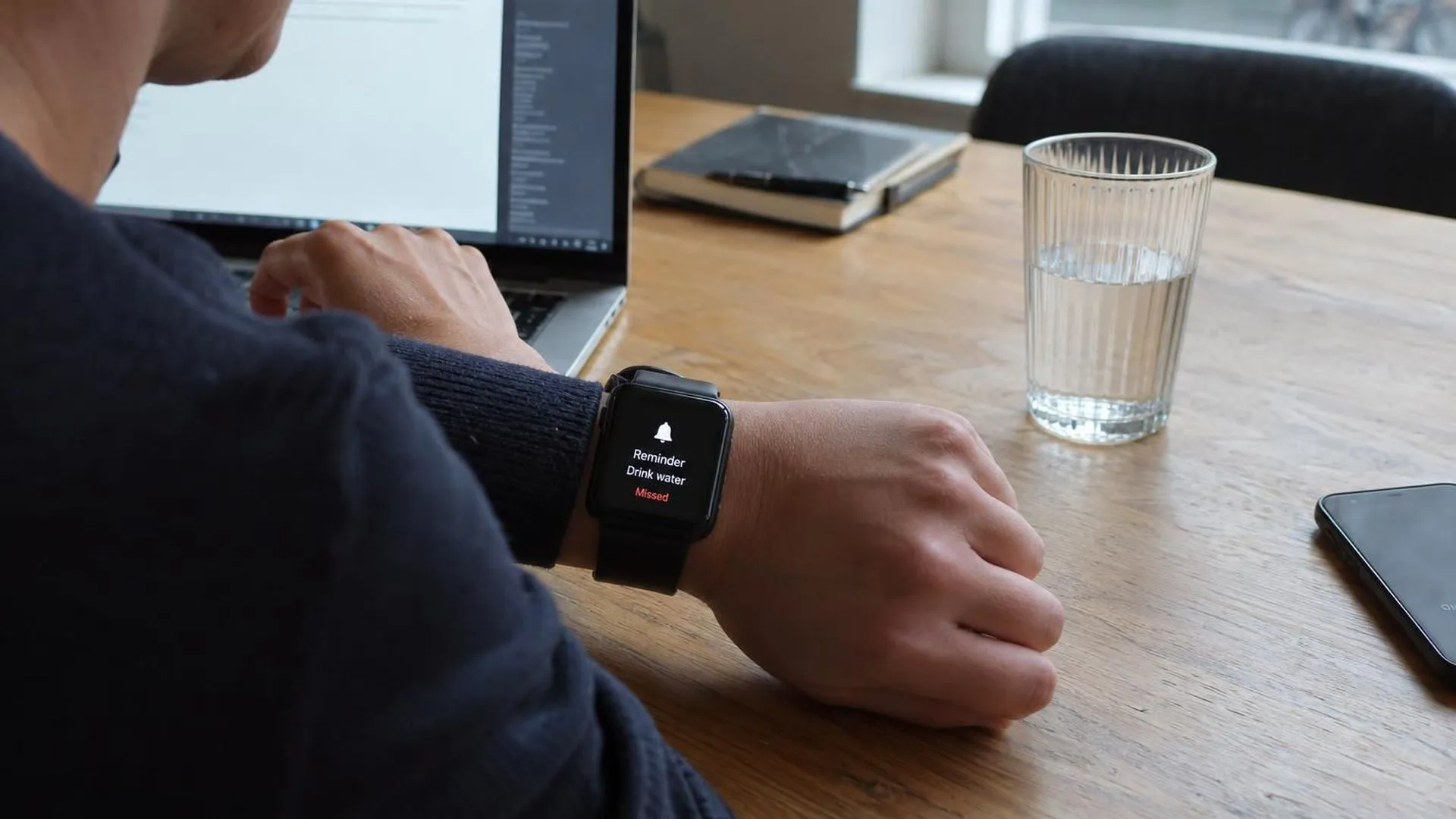 Een smartwatch met een gemiste herinnering, naast een onaangeroerd glas water op een bureau