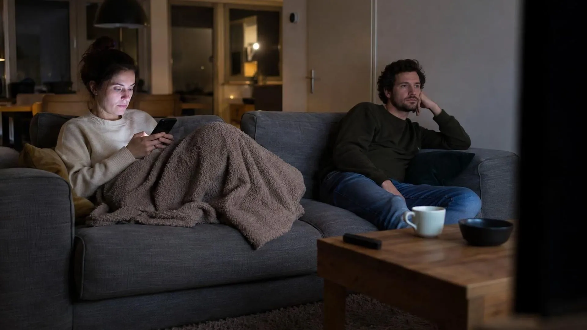 Twee partners aan weerszijden van de bank, ieder in zichzelf gekeerd, in de avond