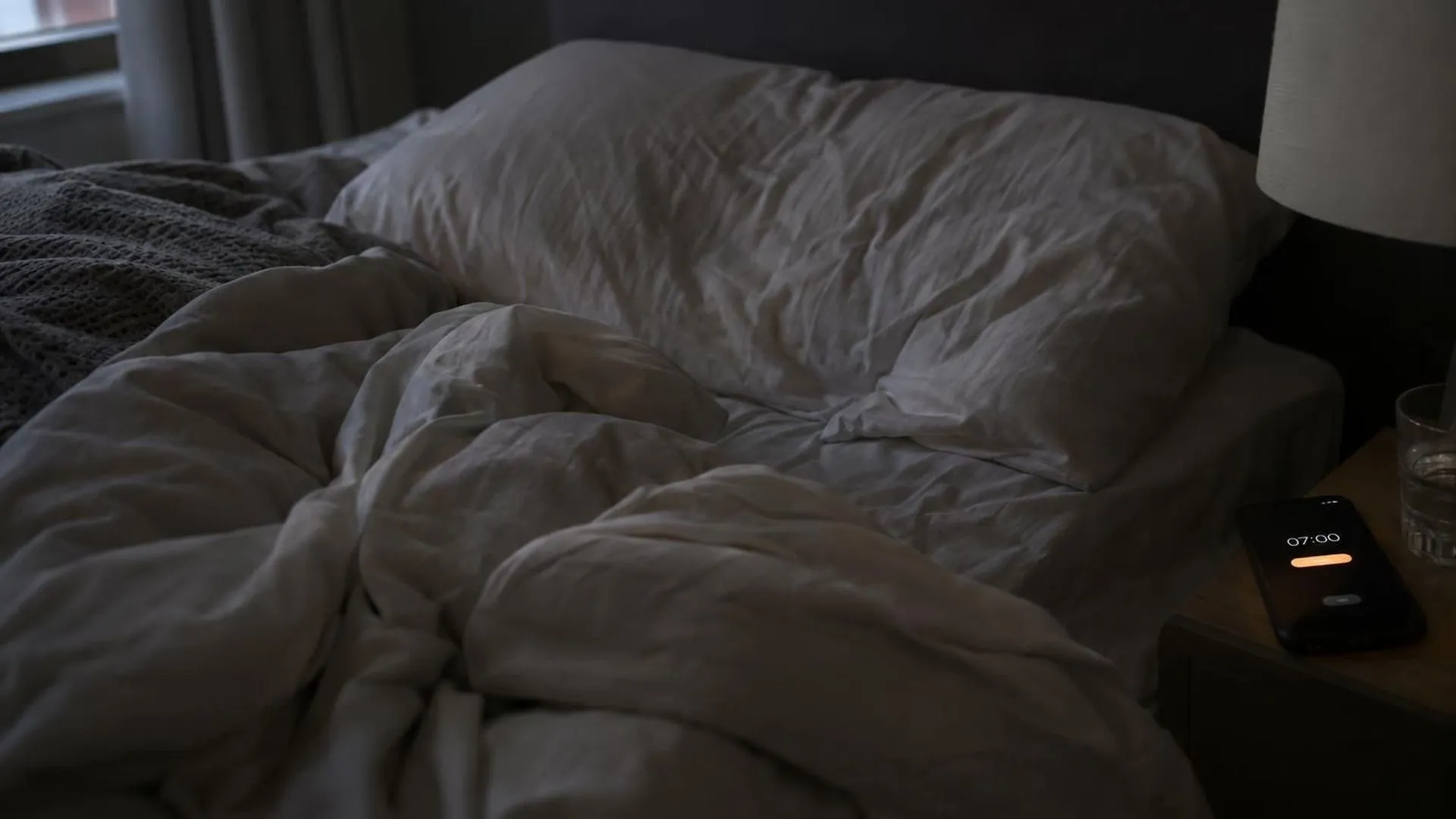 Close-up van verkreukelde lakens en een ingedeukt kussen op maandagochtend, het beeld van wakker worden terwijl je al moe bent.