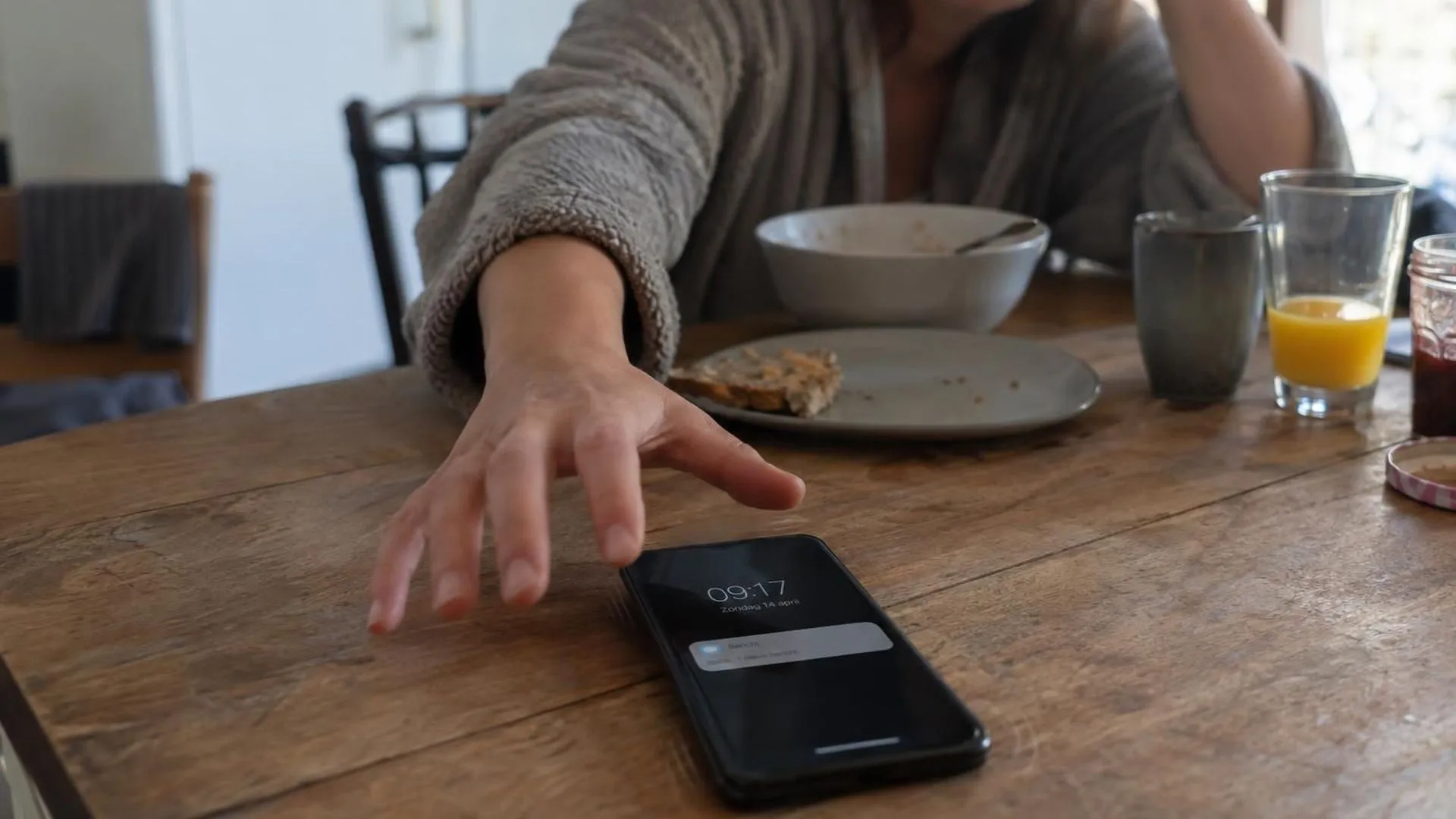 Hand die op zondagochtend naar een trillende telefoon grijpt, ontbijt blijft onaangeroerd