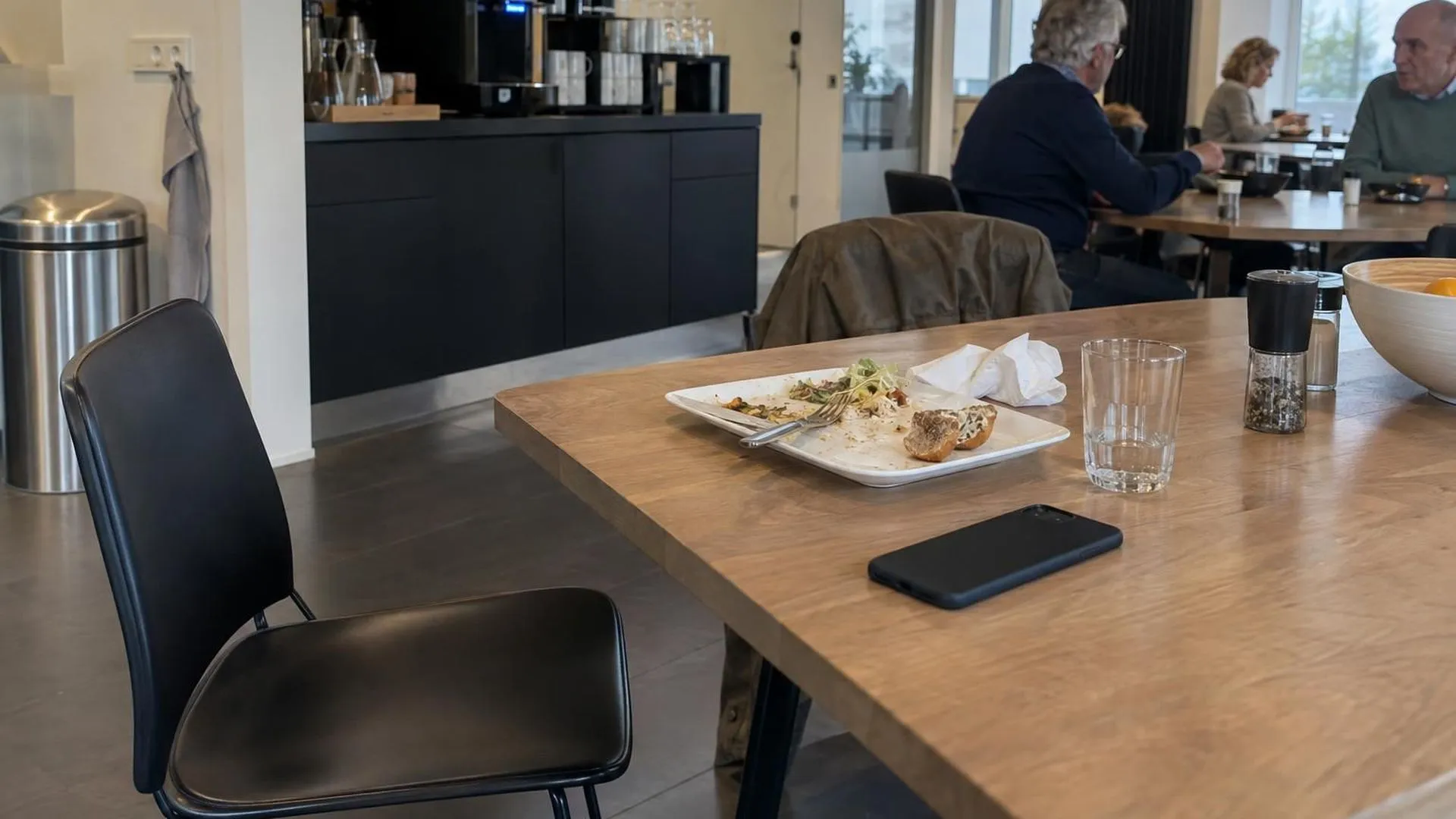 Een halfopgegeten lunch op een pauzetafel op kantoor, met een omgekeerde telefoon ernaast en een weggeschoven stoel
