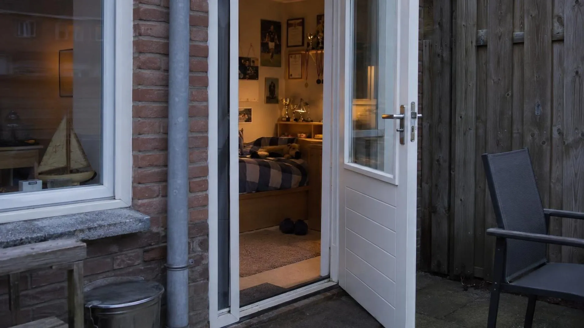 De deur van een kinderslaapkamer staat op een kier, met oude diploma's en bekers nog aan de muur, gangverlichting valt naar binnen
