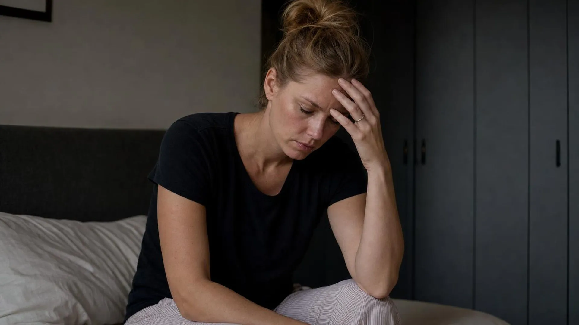 Vrouw zit op rand van bed en houdt haar hoofd vast door duizeligheid bij stress