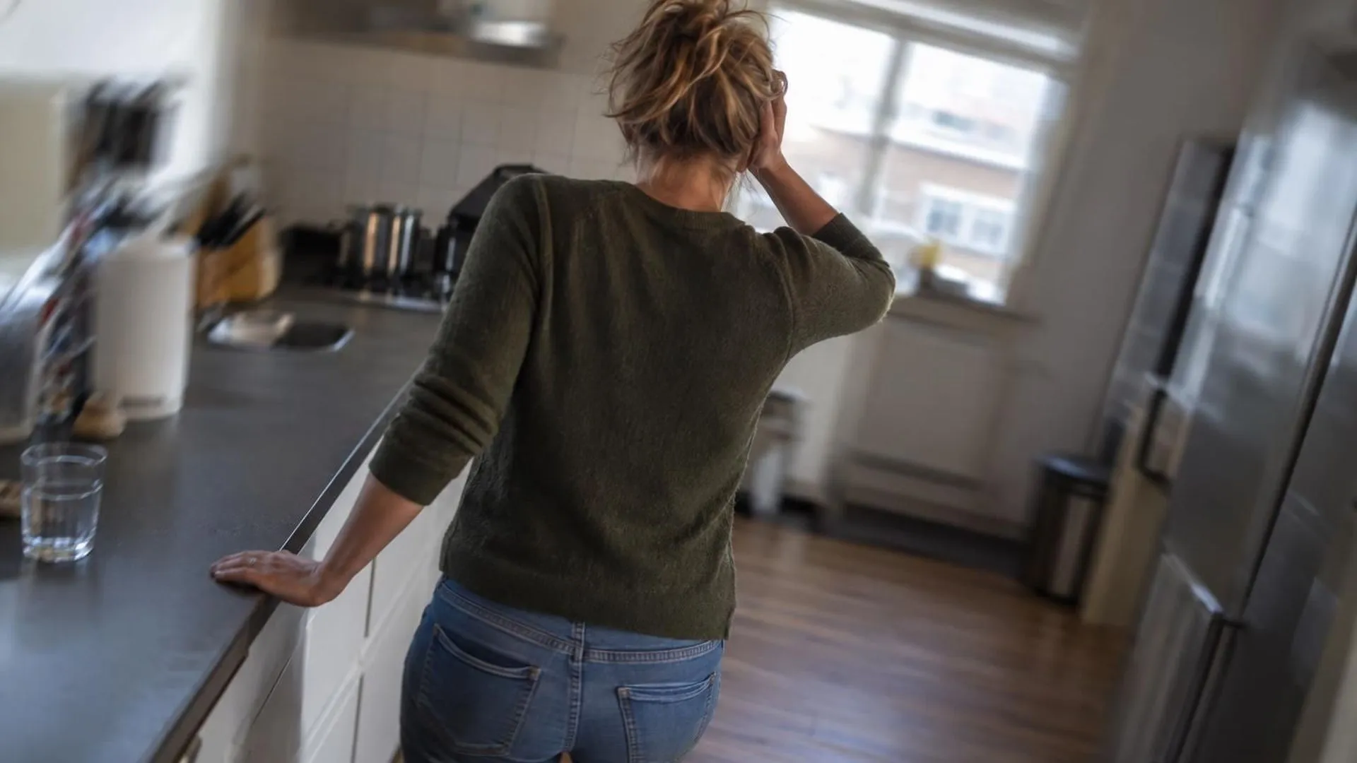 Iemand van achteren gefotografeerd met een hand op het aanrecht om steun te zoeken, de ruimte licht wazig alsof het draait.