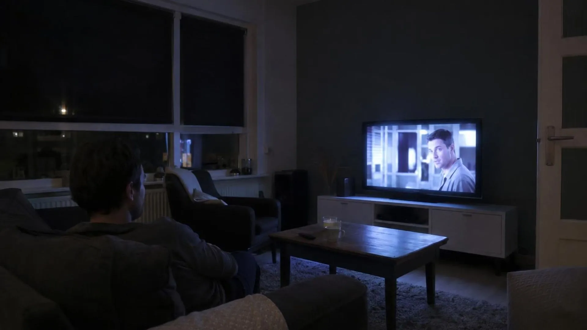 Een huiskamer die alleen verlicht wordt door het flakkerende licht van de televisie, een stille schaduw op de bank