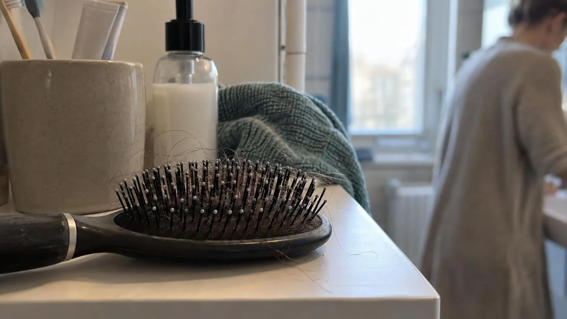 Close-up van een haarborstel op een badkamerplankje met haarstrengen in de borstelharen, ochtendlicht.