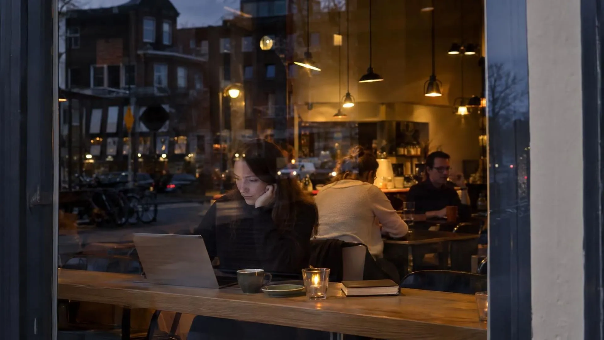 Een caféraam bij schemering waarin straatbeeld en interieur door elkaar heen weerspiegelen.