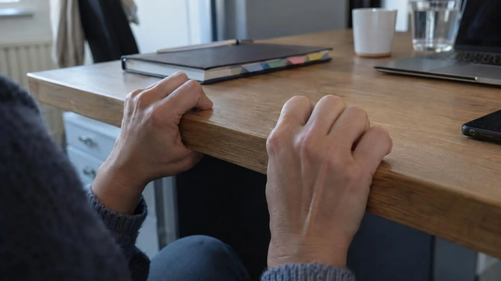 Handen die de rand van een bureau vastgrijpen, terwijl een keurig bijgehouden agenda ernaast ligt