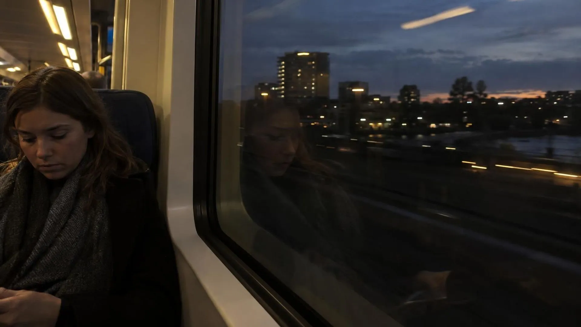 Een vage spiegeling van iemand in het donkere raam van een trein bij schemering
