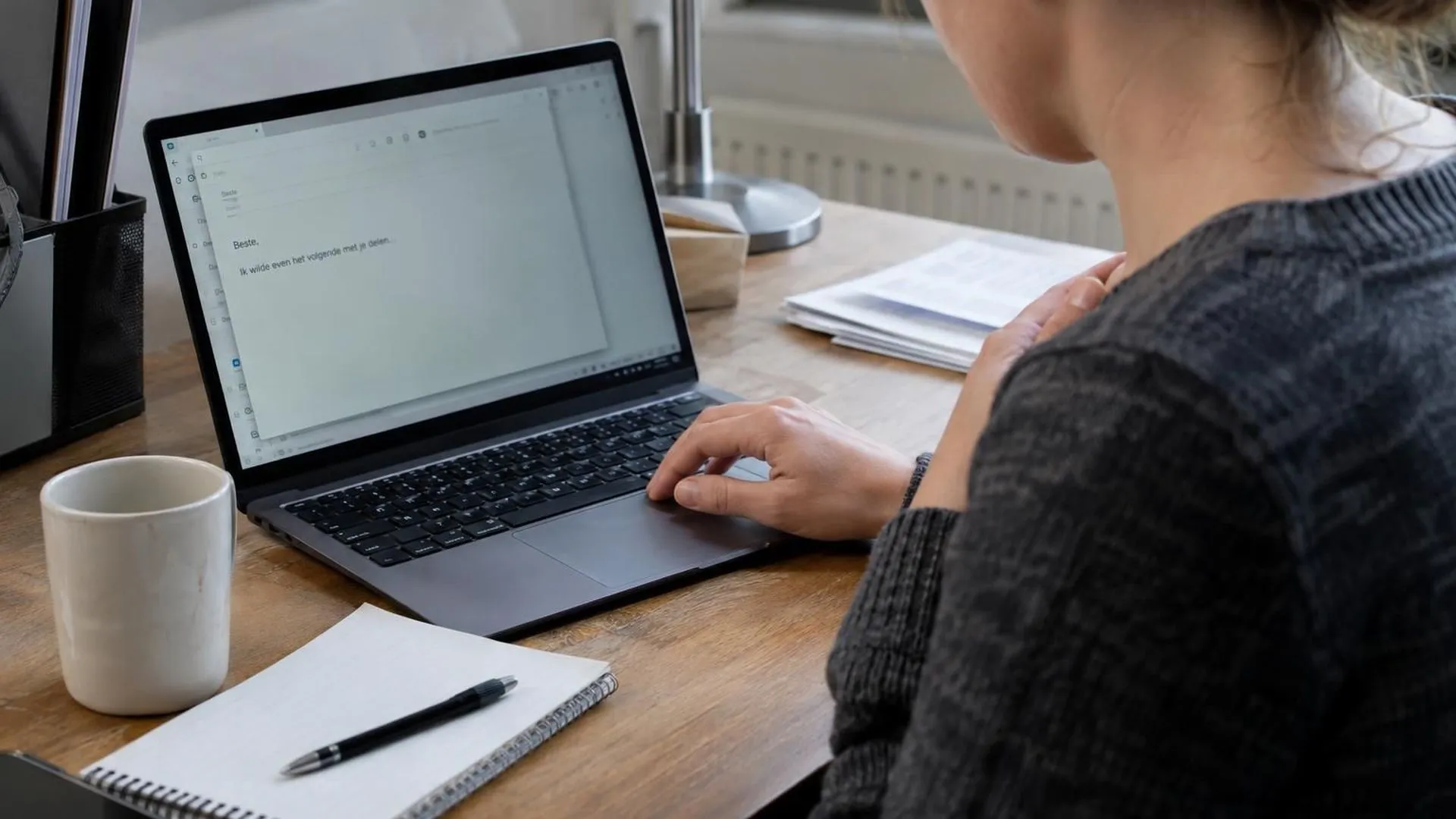 Handen boven een toetsenbord, een hand kort tegen de borst, met een onafgemaakte e-mail op het scherm