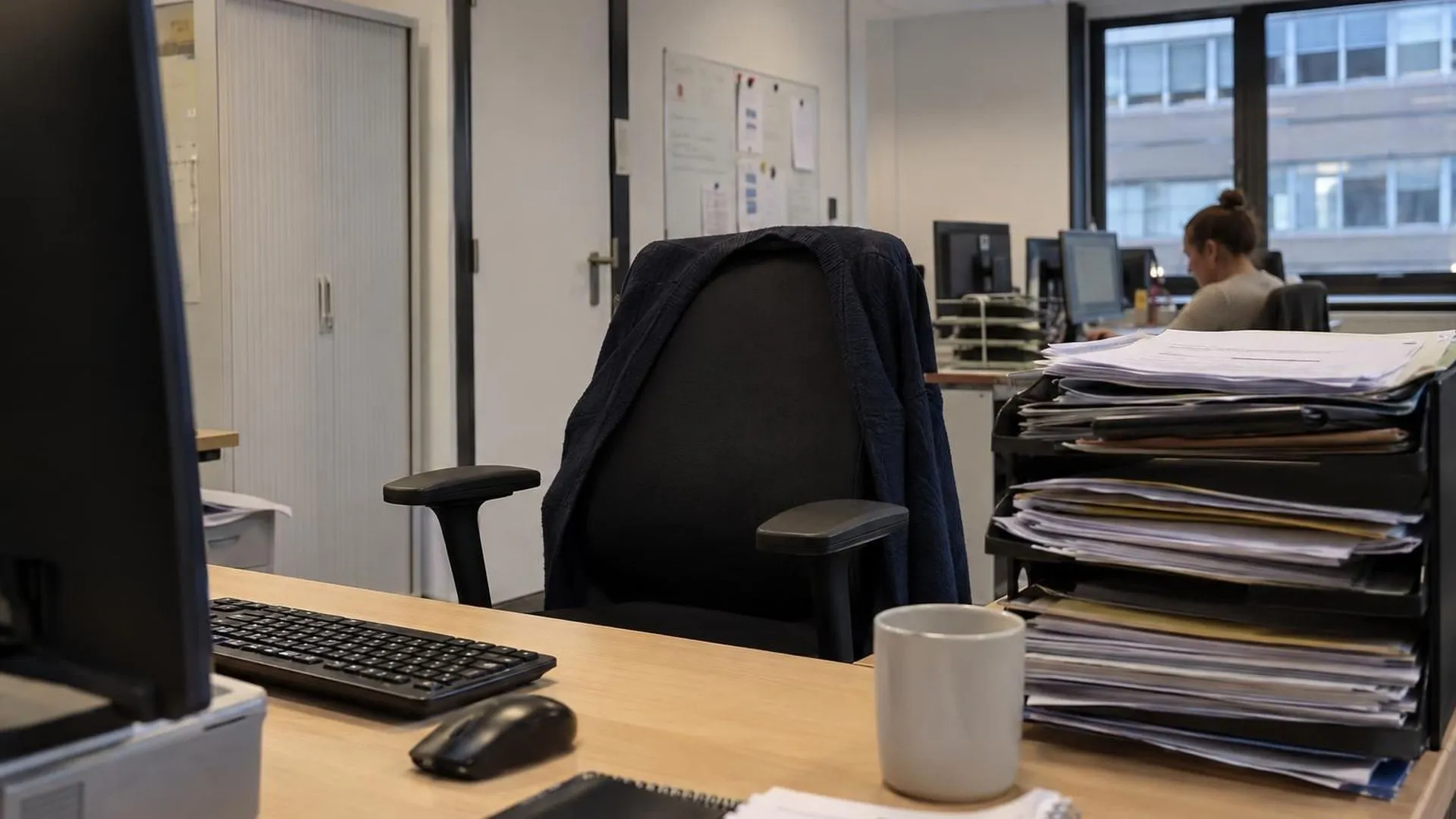 Een lege bureaustoel naast een overvolle intake-bak op kantoor