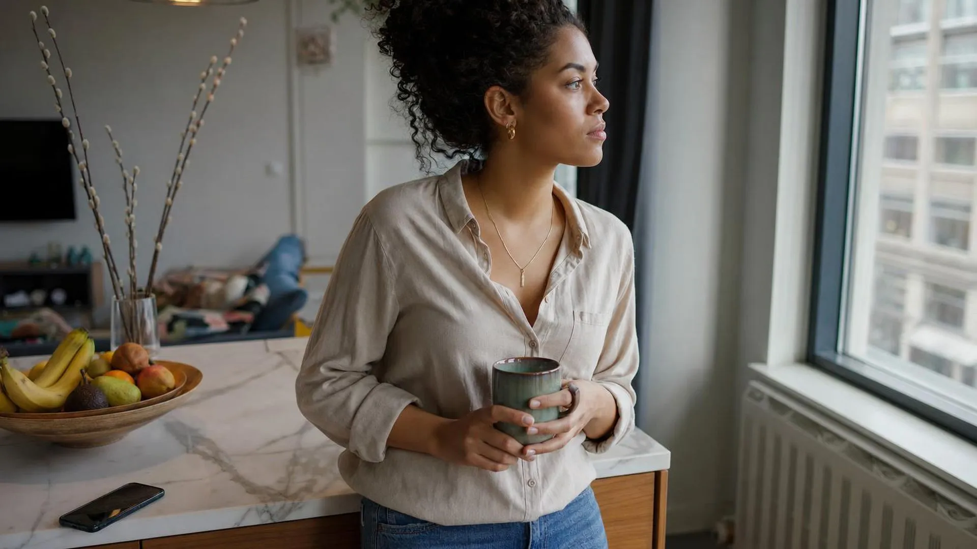 Persoon staat met koffie in de hand bij het keukenblad en kijkt naar buiten