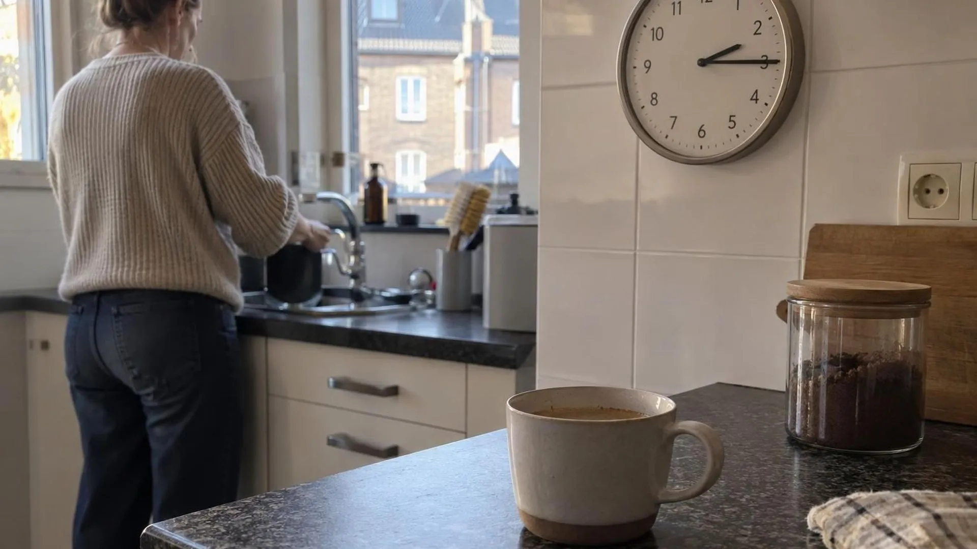 Een half leeg koffiekopje naast een klok die kwart over twee aangeeft op het aanrecht