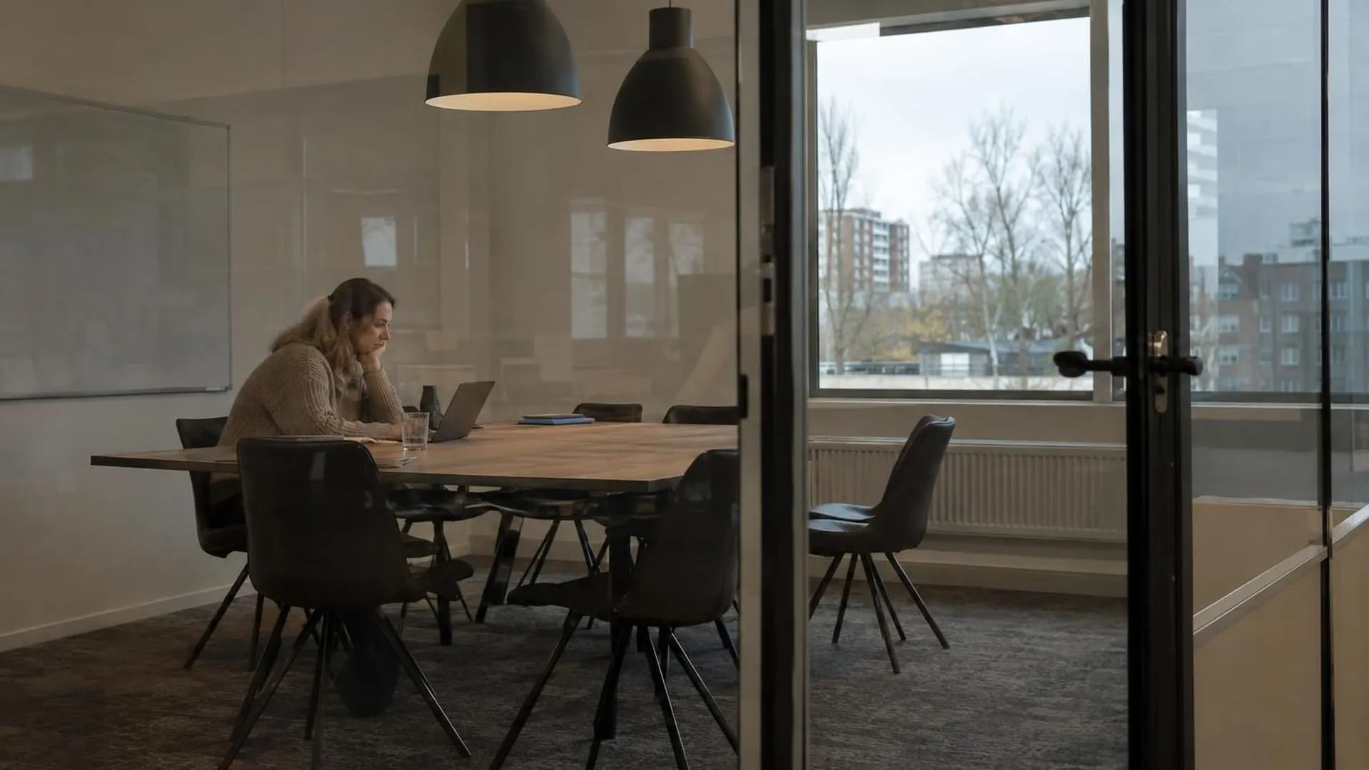 Door het glas van een vergaderkamer gezien blijft één figuur achter nadat iedereen is vertrokken.