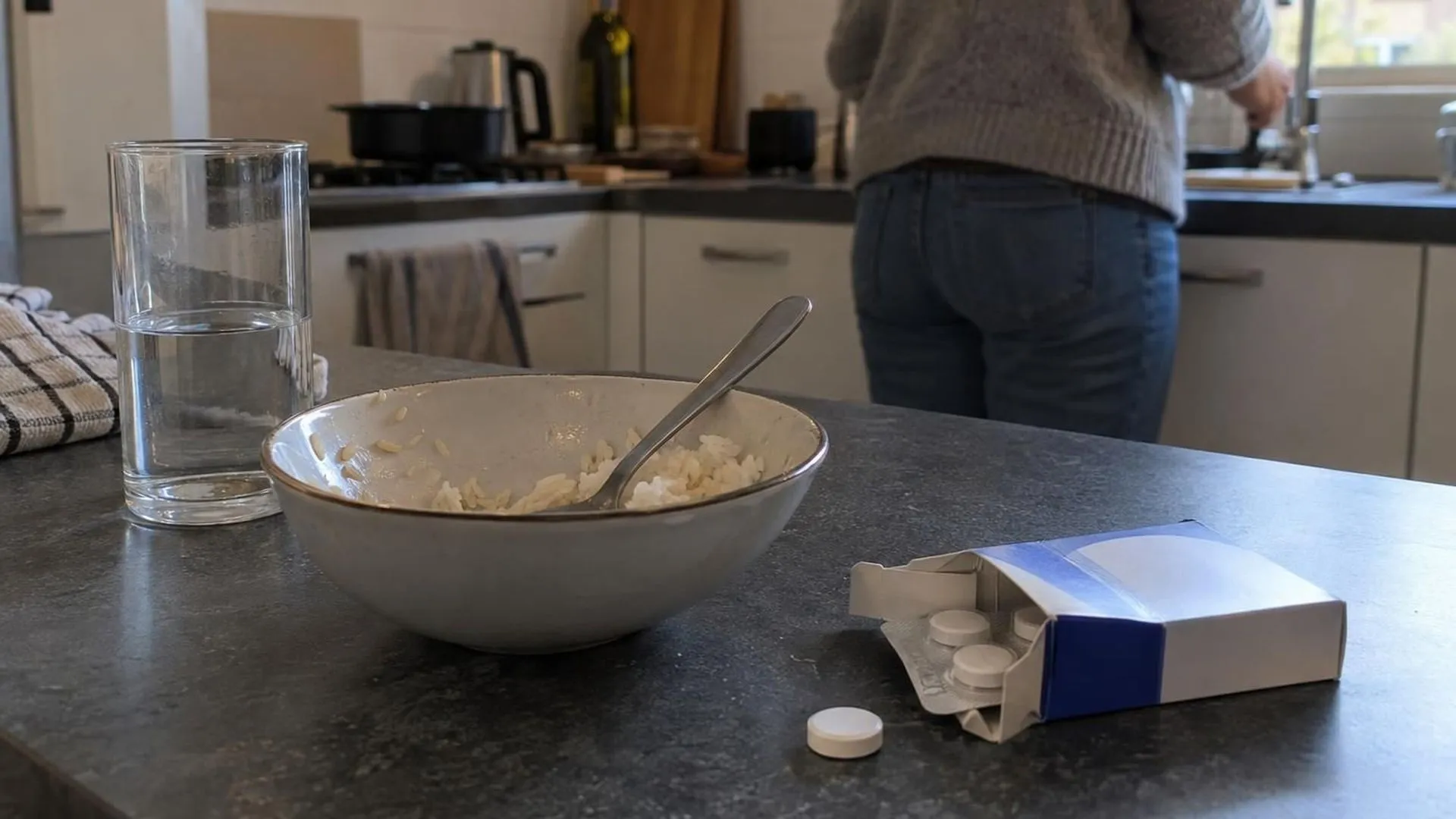 Een half opgegeten bord met eenvoudige rijst naast een doosje maagzuurremmers op het aanrecht