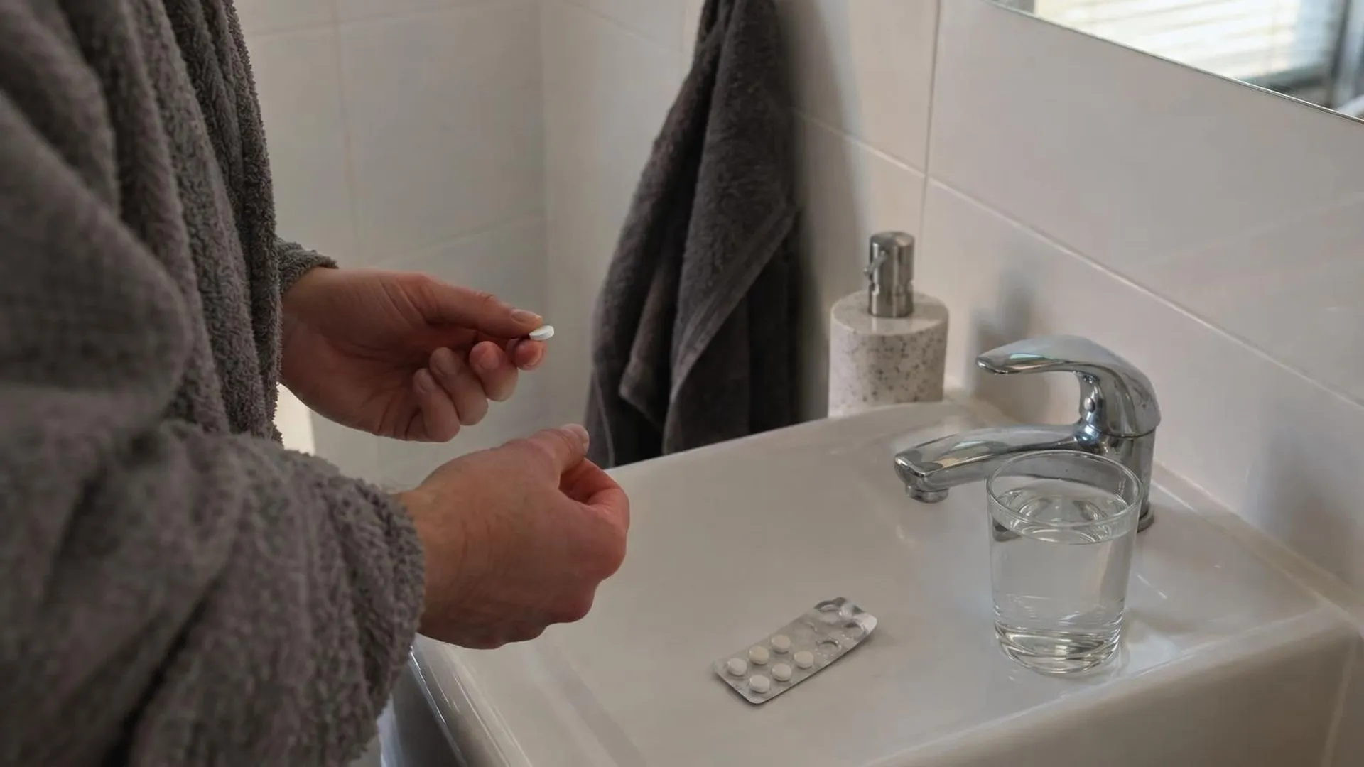 Een strip pillen naast een vol glas water op de badkamerwastafel