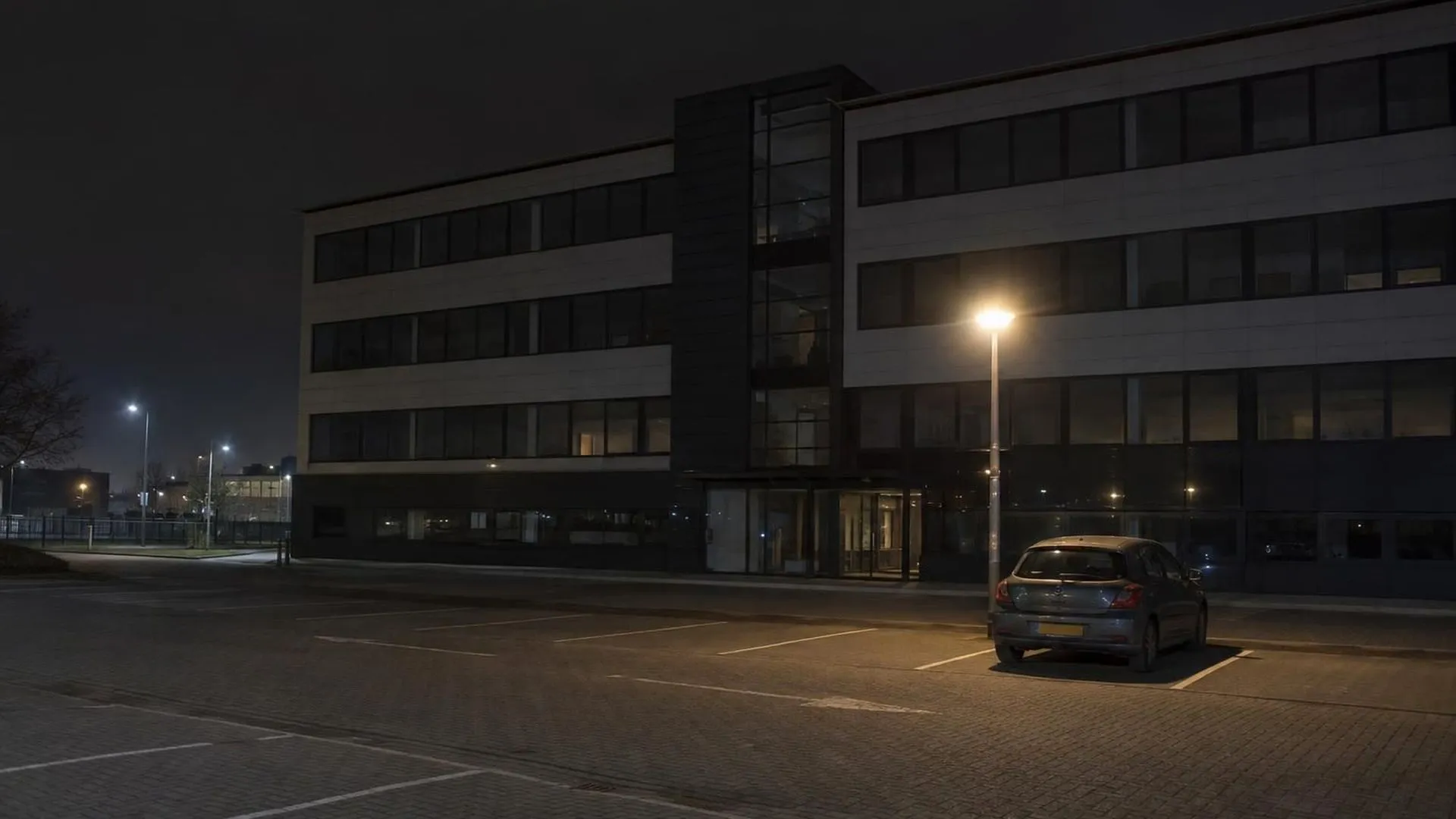 Een verlaten kantoorparkeerplaats op zondagavond met nog maar één auto onder een lantaarn
