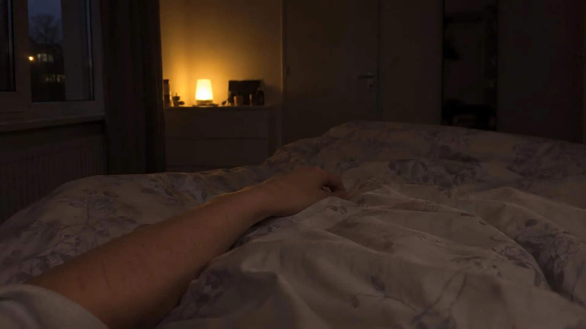 Een schemerige slaapkamer 's nachts met een blote onderarm met lichte krasplekken zichtbaar bij het dekbed.