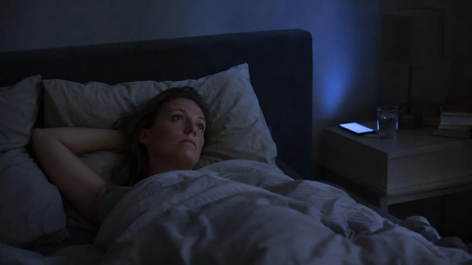 Iemand ligt wakker in een donkere slaapkamer, het schijnsel van een telefoon werpt licht op het plafond