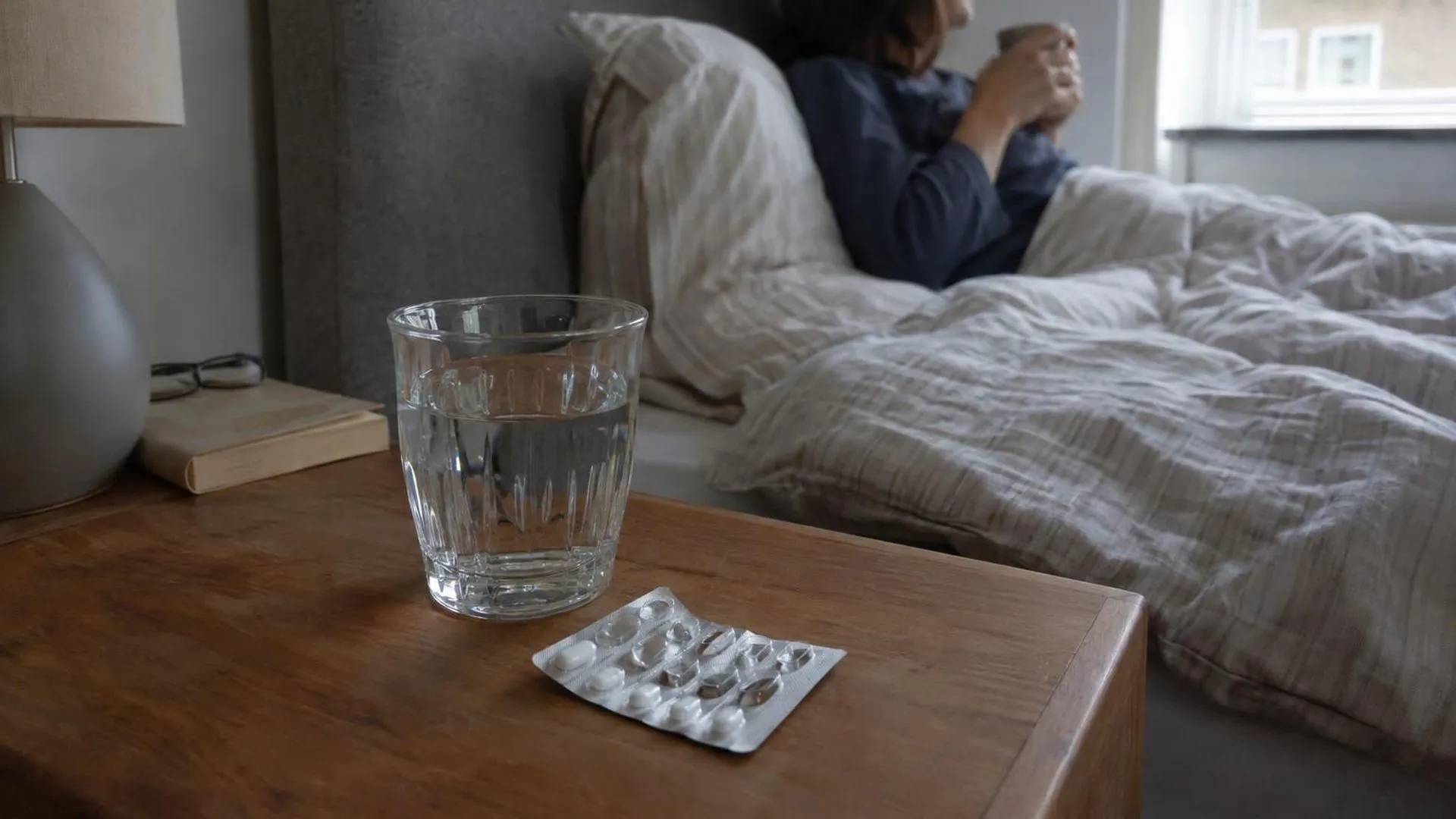 Een strip medicijnen en een vol glas water op een nachtkastje in het rustige ochtendlicht