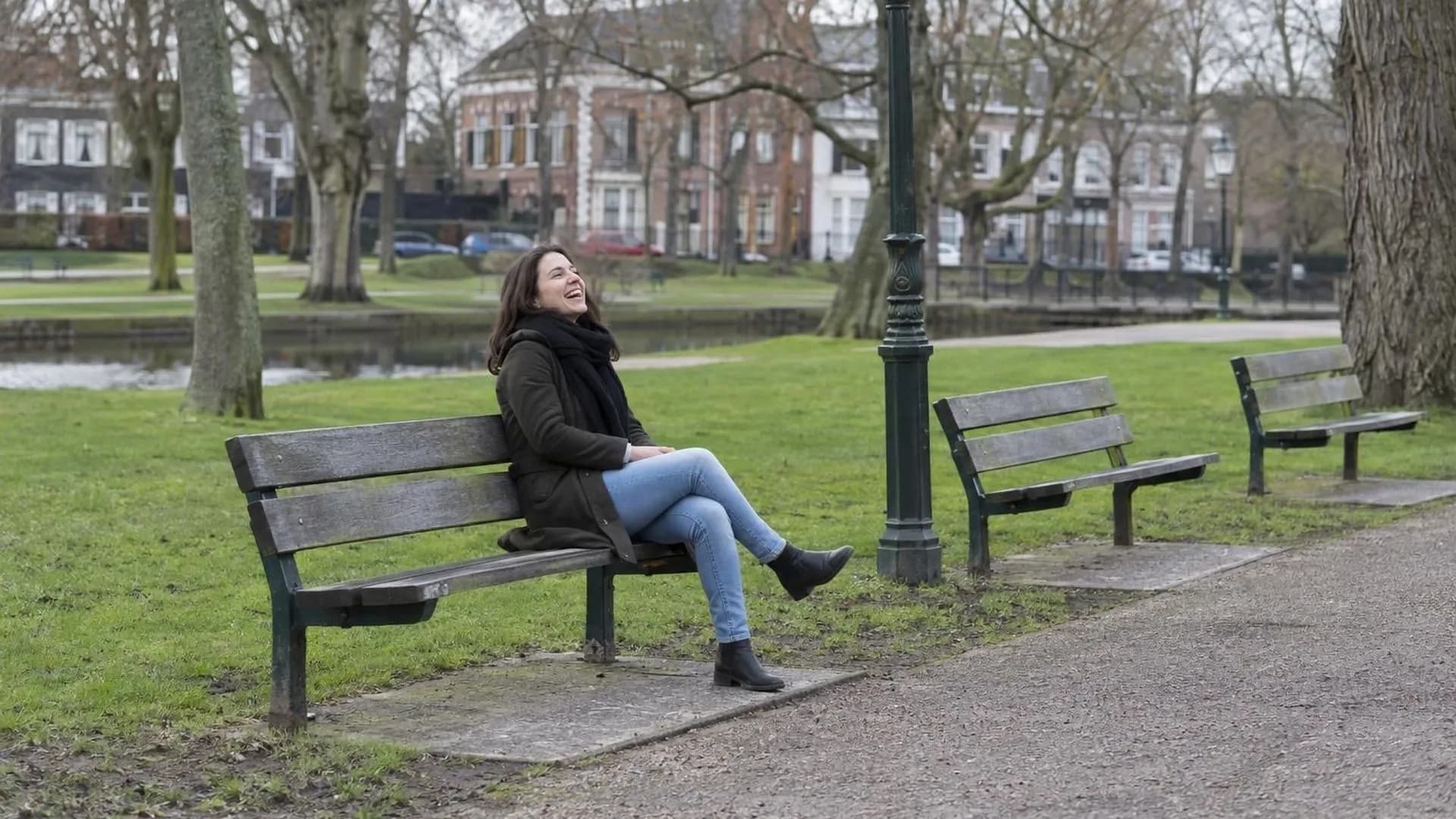 Iemand lacht alleen op een bankje in een park, de andere bankjes eromheen zijn leeg