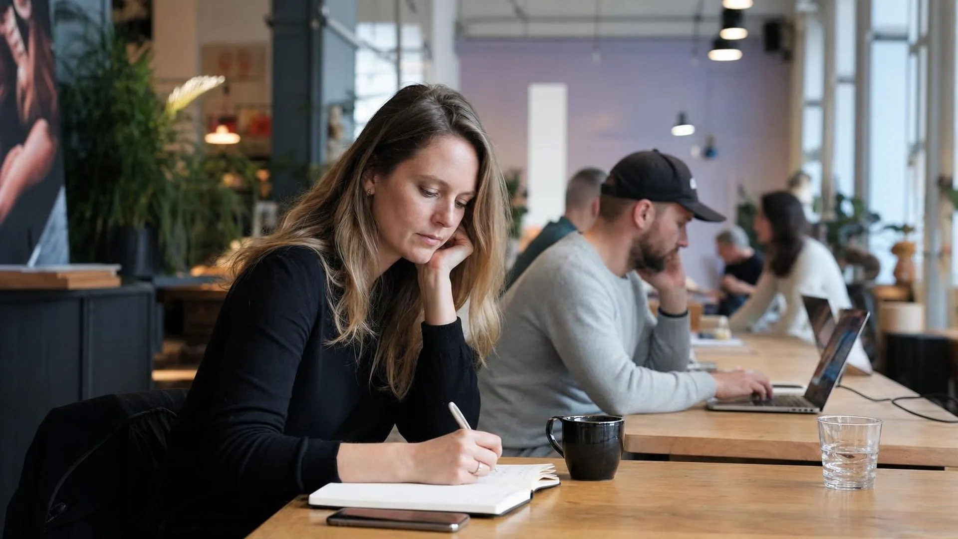 Persoon zit aan een grote tafel en kijkt peinzend naar een notitieboek
