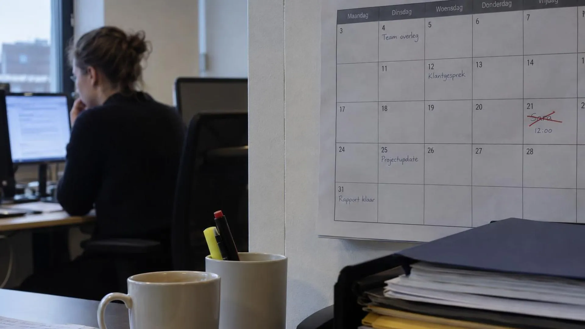 Een wandplanner op kantoor met een naam die in rood is doorgestreept op de datum van vandaag.