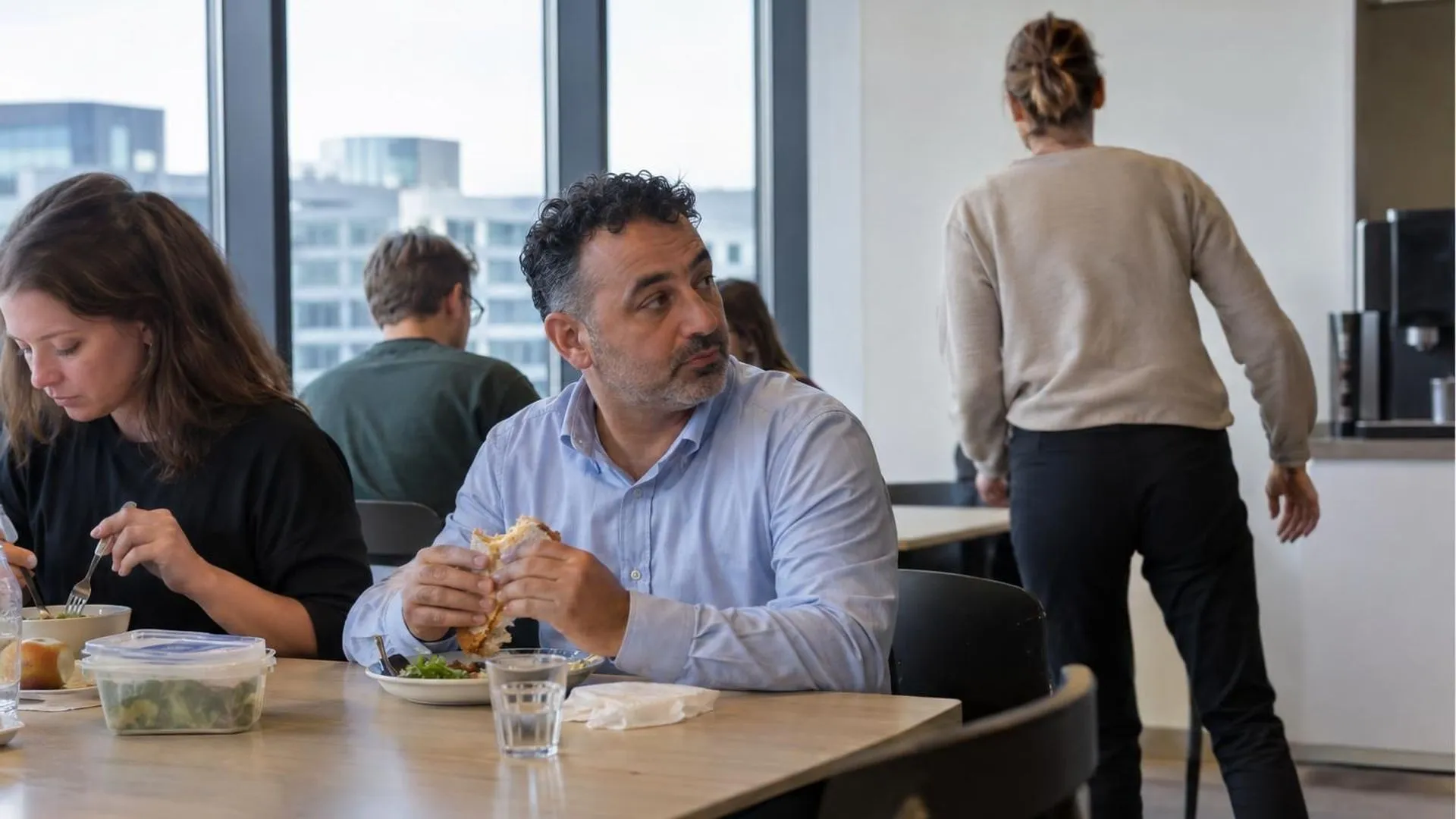 Een lunchtafel op kantoor, iemand kijkt weg terwijl een collega opstaat en wegloopt