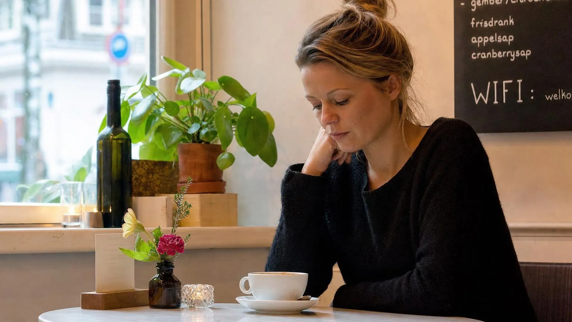 Persoon zit alleen aan een cafétafel en kijkt naar een onaangeroerd kopje koffie