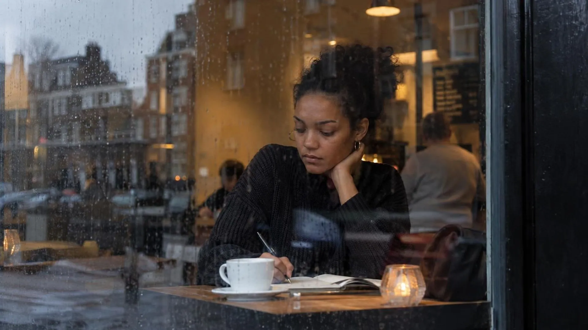 Iemand gezien door een beregend caferaam, alleen aan een tafeltje binnen