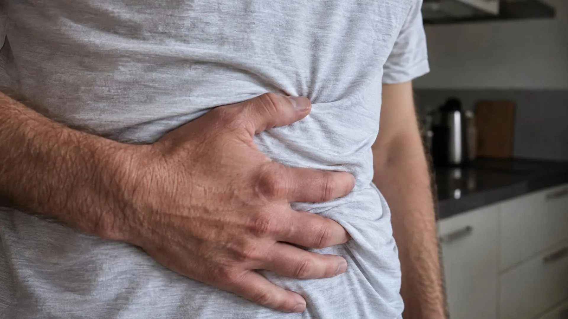 Close-up van een hand die tegen de buik drukt door een gekreukeld shirt heen