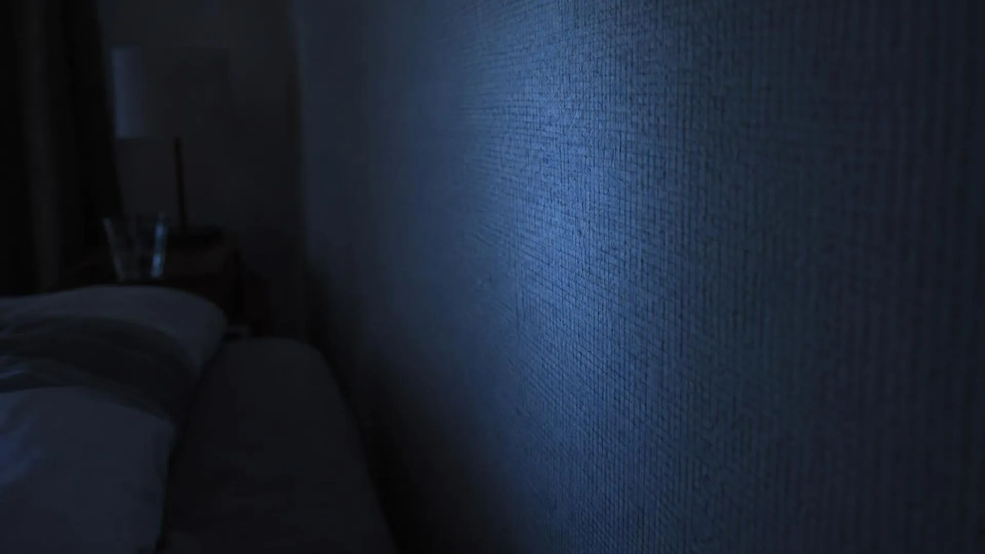 Blauw schermlicht van een telefoon weerkaatst op een muur in een donkere slaapkamer