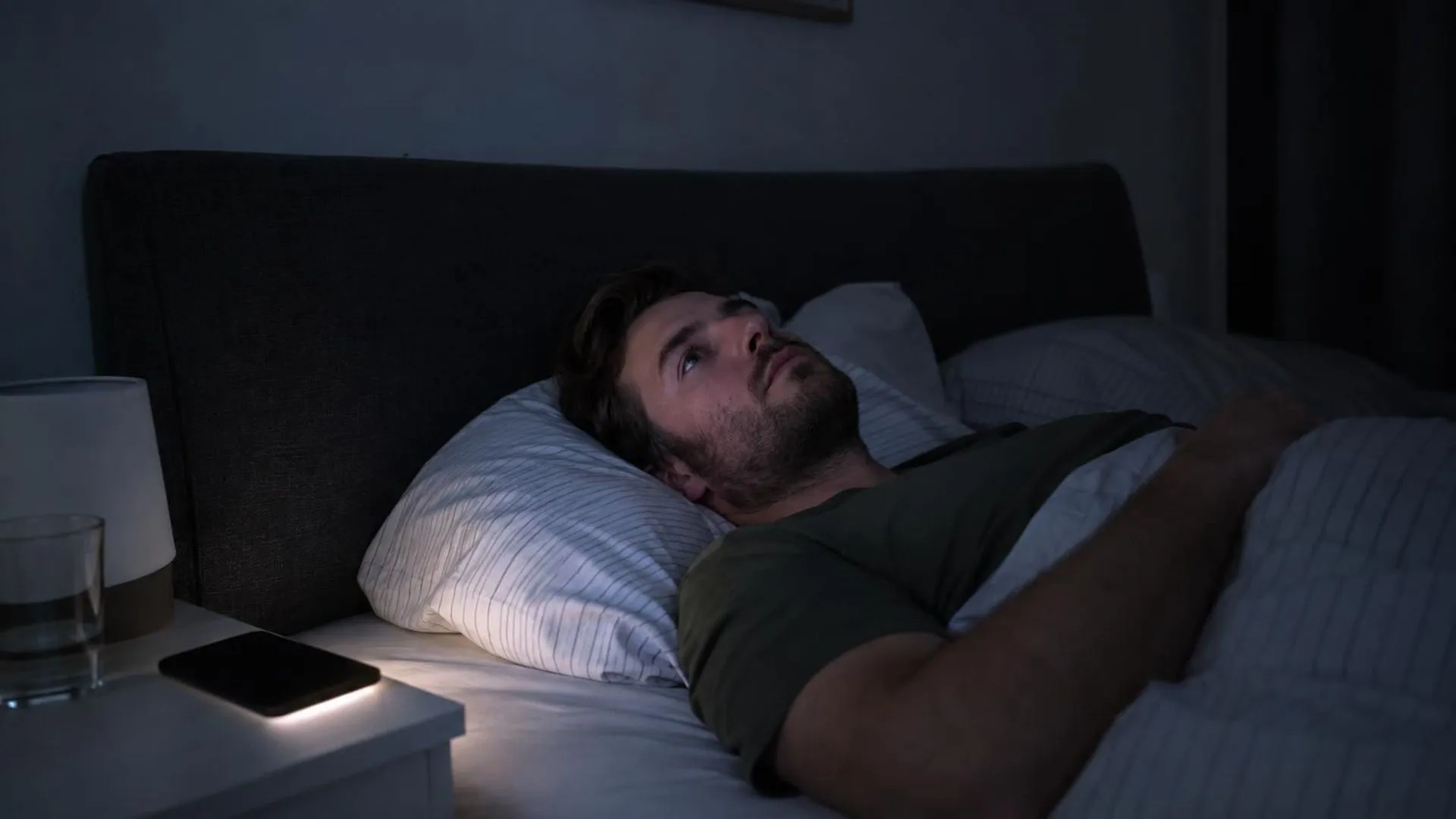 Iemand ligt wakker in bed in het donker, met alleen het gloeien van een telefoon naast het kussen