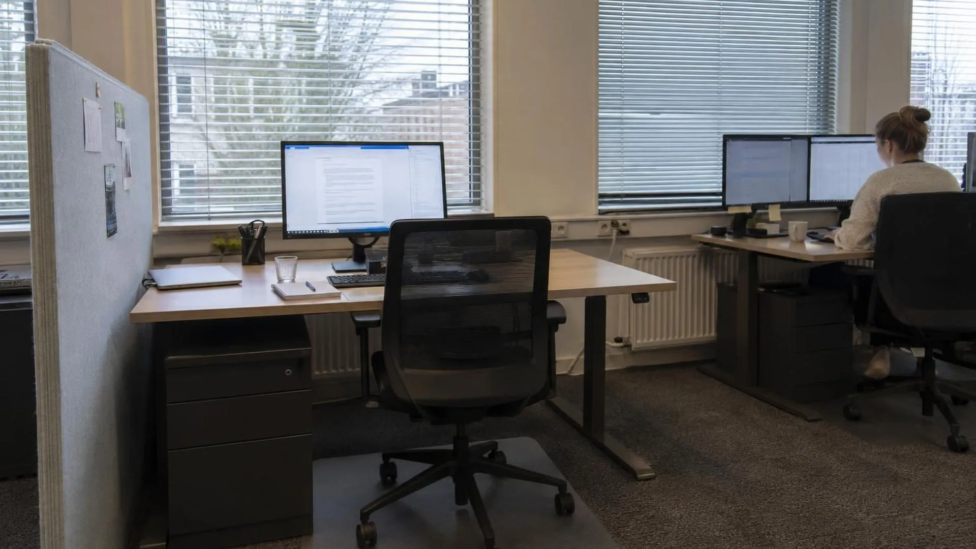 Lege bureaustoel bij een opgeruimd bureau met brandend scherm, naast een wel bezet bureau, maandagochtend