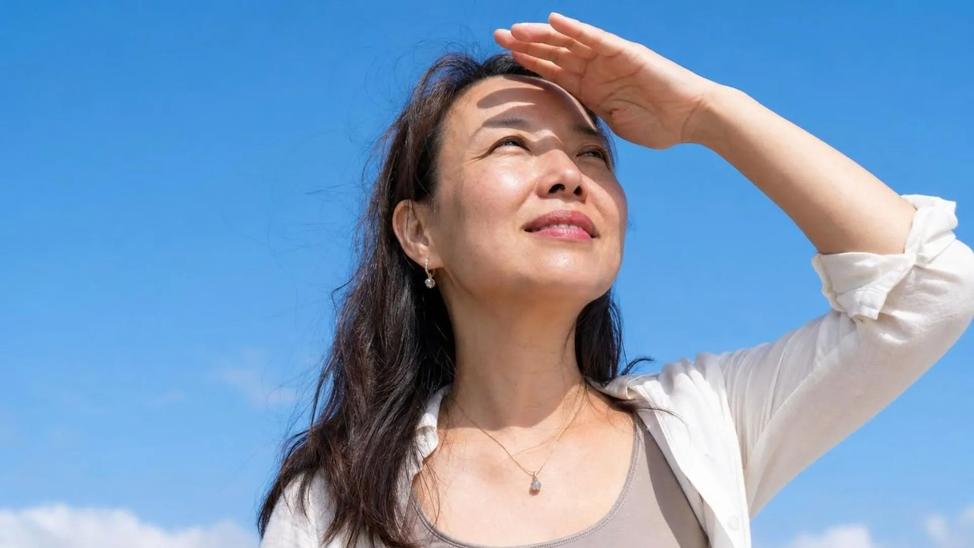 Iemand kijkt met de hand boven de ogen naar een heldere lichte lucht