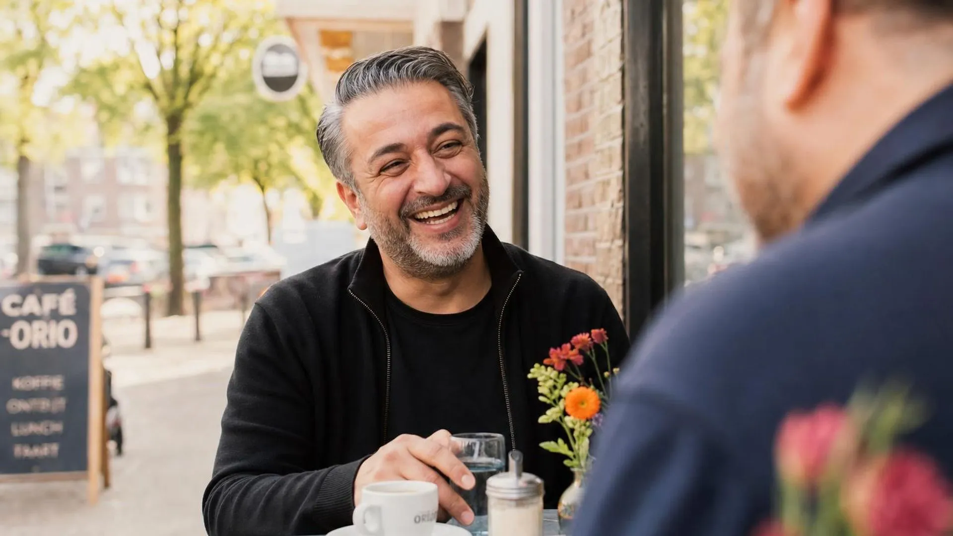 Twee mensen lachen samen aan een tafeltje op een stadsterras