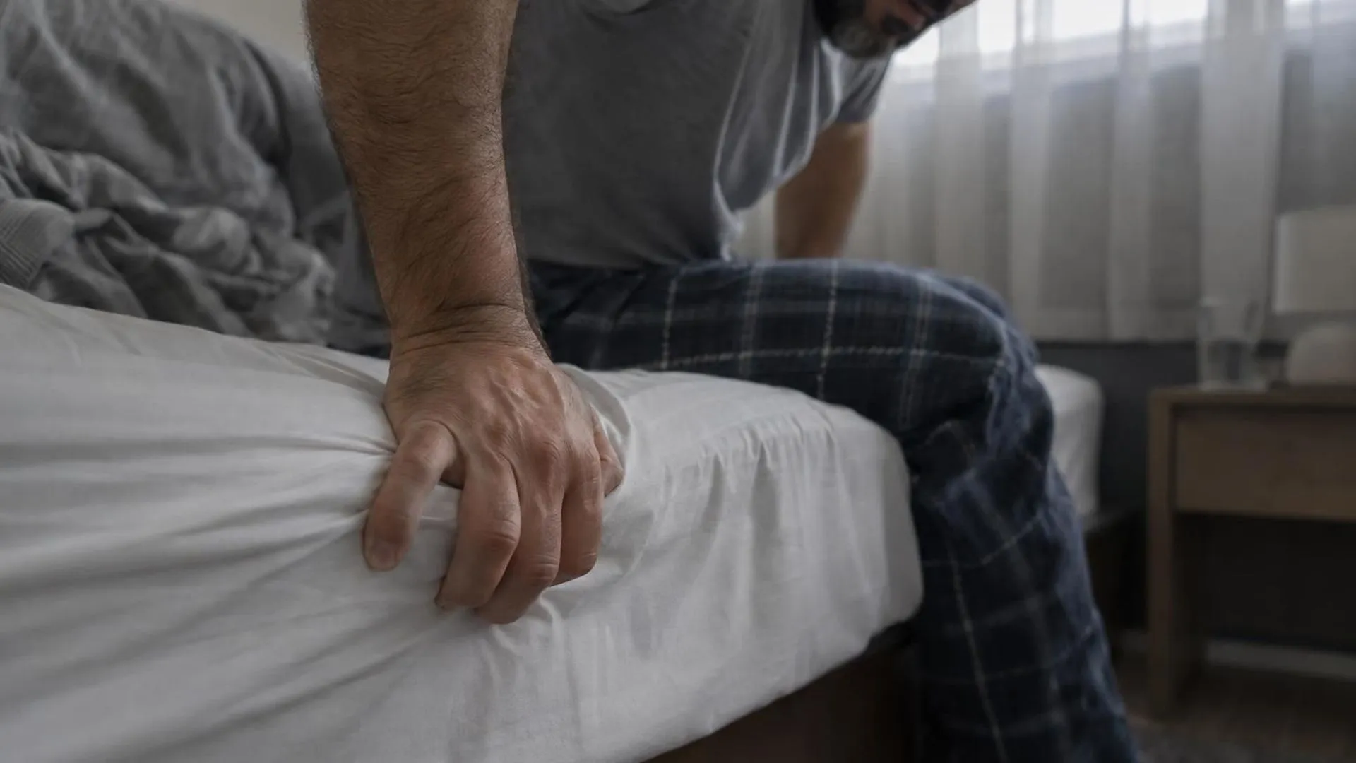 Close-up van een hand die zwaar op de rand van het bed steunt om overeind te komen, het lichaam van iemand die na het slapen nog steeds op is.