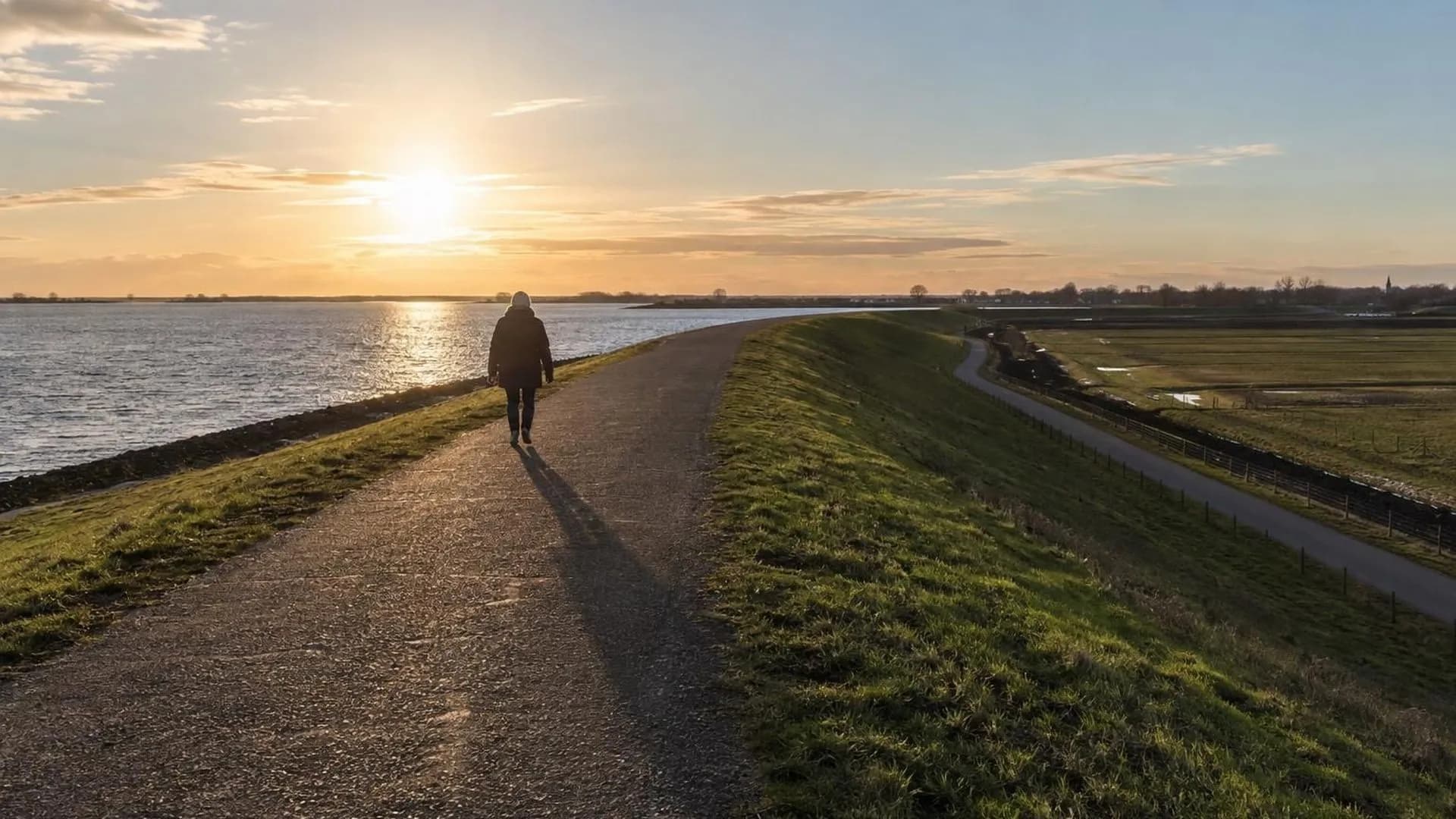 Klein figuur op een breed Nederlands dijkpad in laag herfstlicht tijdens een wandeling