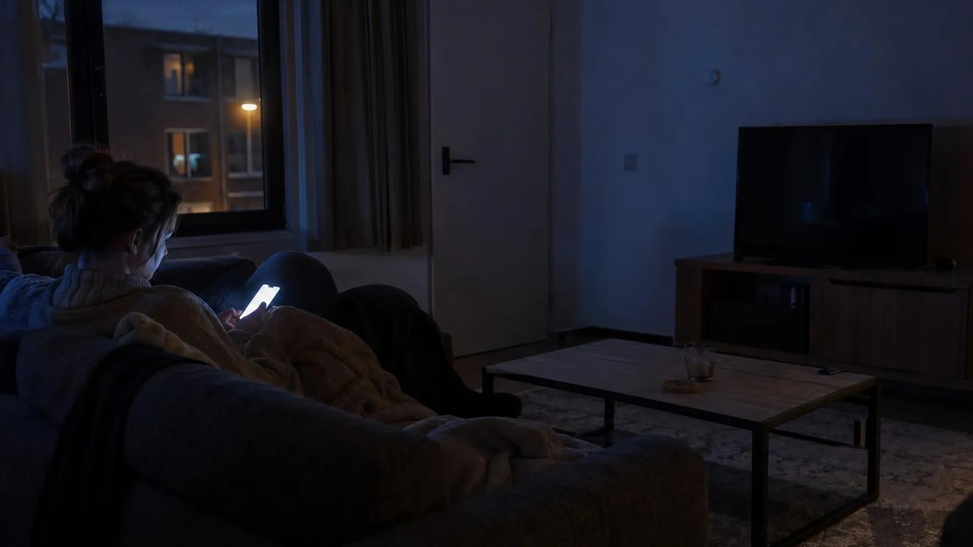 Oplichtende telefoon op de bank in een donkere huiskamer, 's avonds na het werk