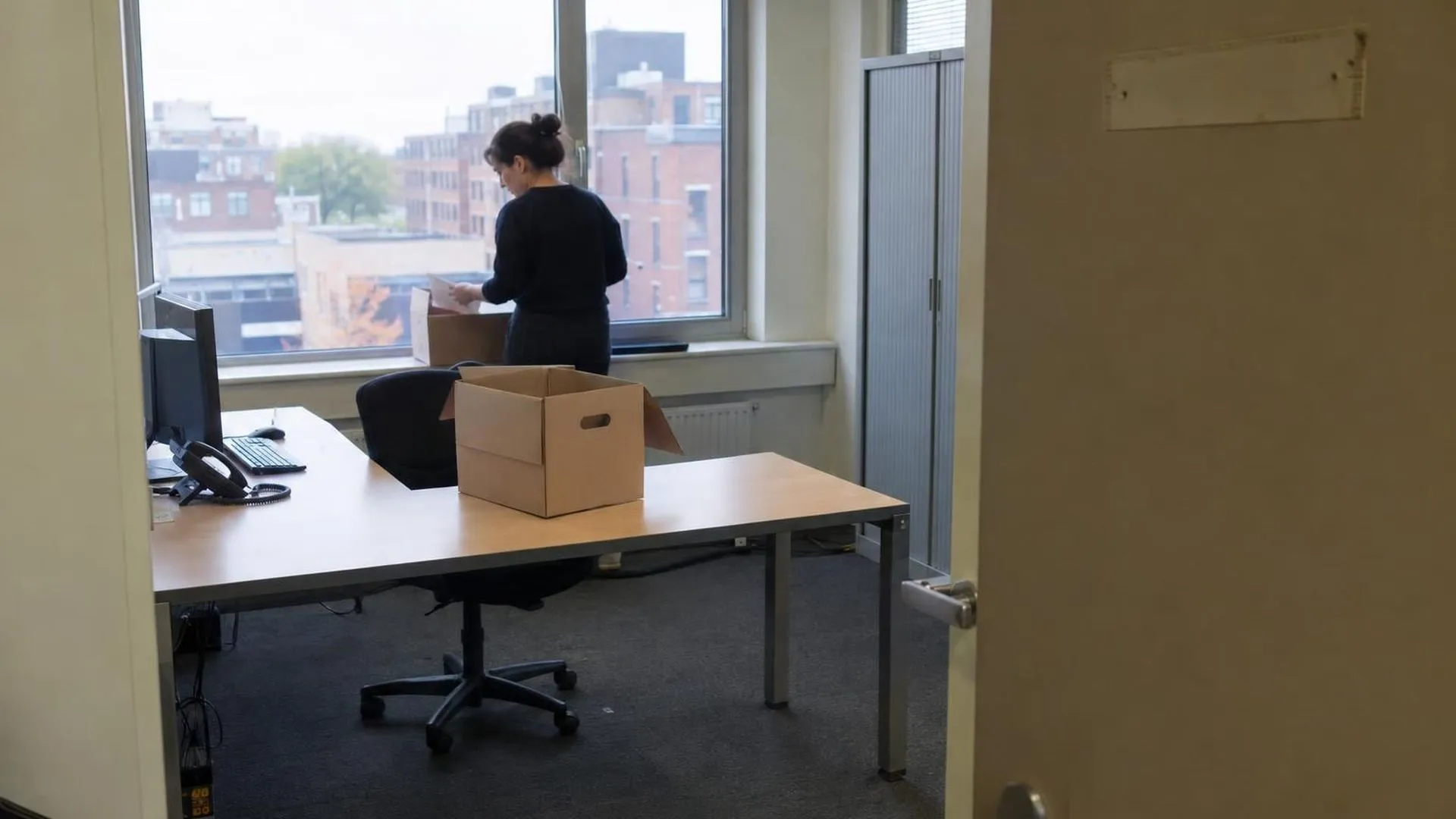 Een leeggeruimd bureau met een verhuisdoos erop, het naamplaatje is al van de deur