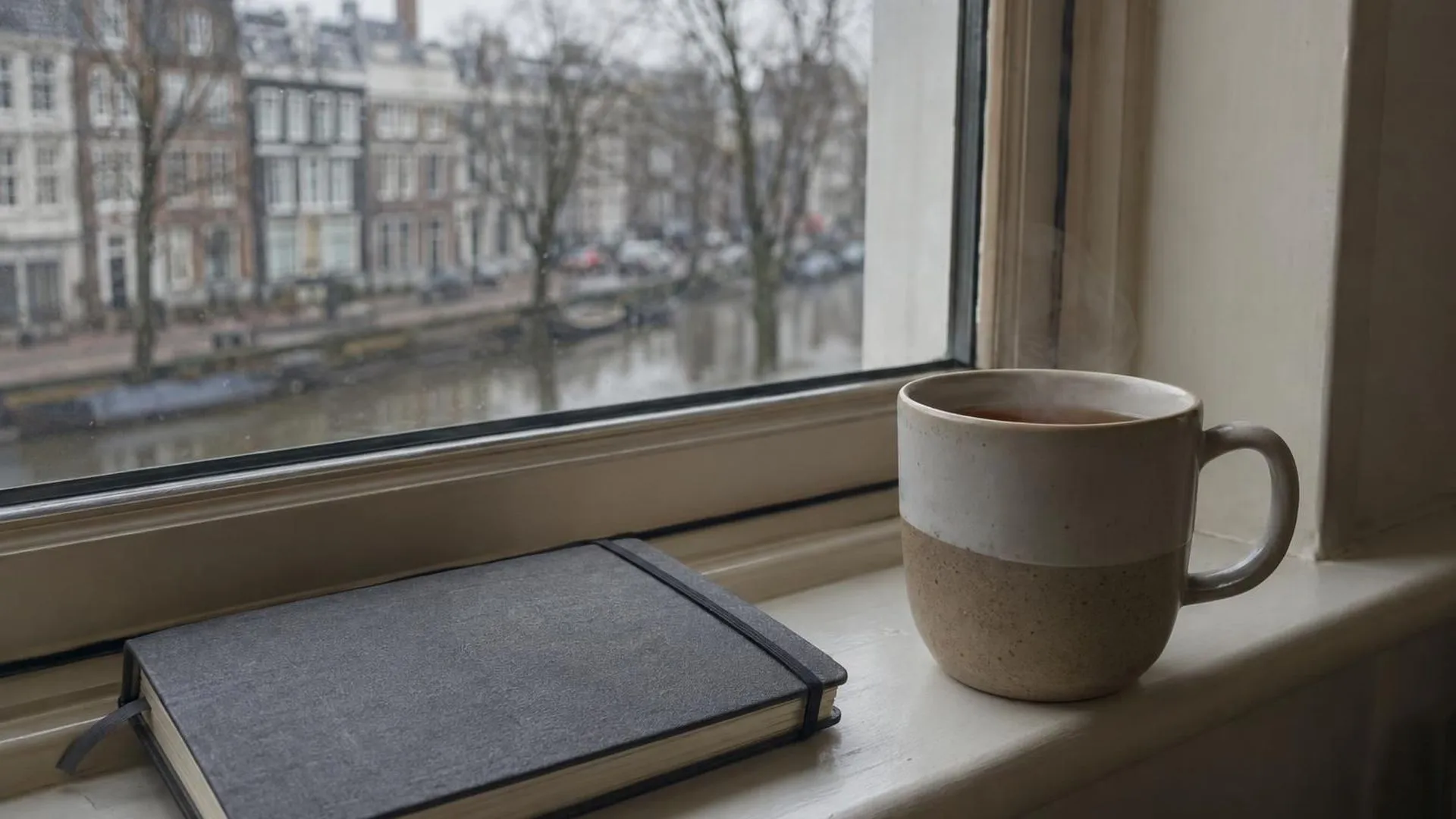 Een dampende mok thee op een vensterbank naast een gesloten agenda, in zacht ochtendlicht.
