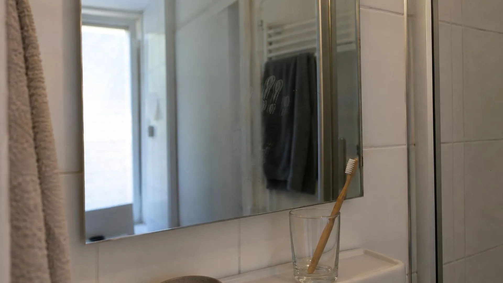 Een badkamerspiegel met een vage handafdruk en een glas met een tandenborstel ernaast, zonder dat er iemand in beeld is.