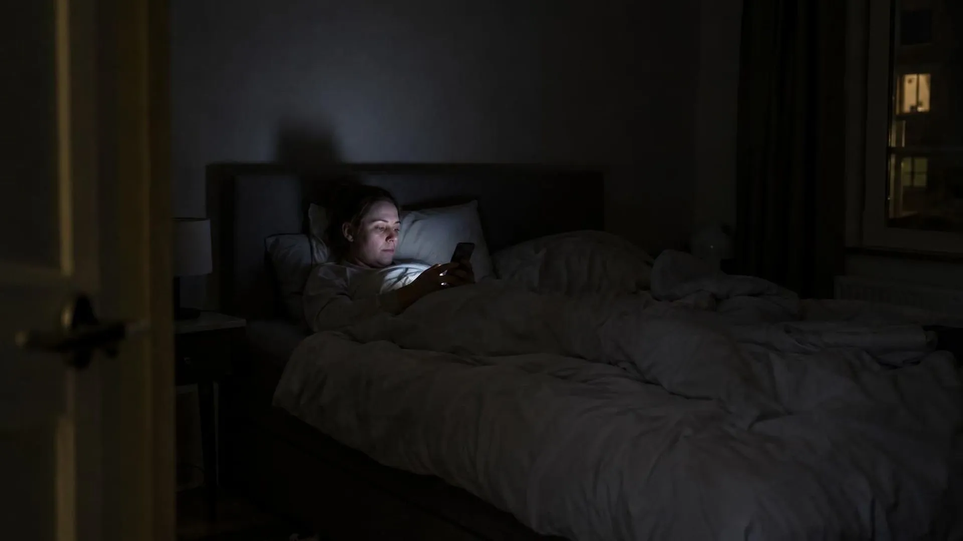 Een telefoonscherm verlicht een gezicht in een donkere slaapkamer, ver na middernacht