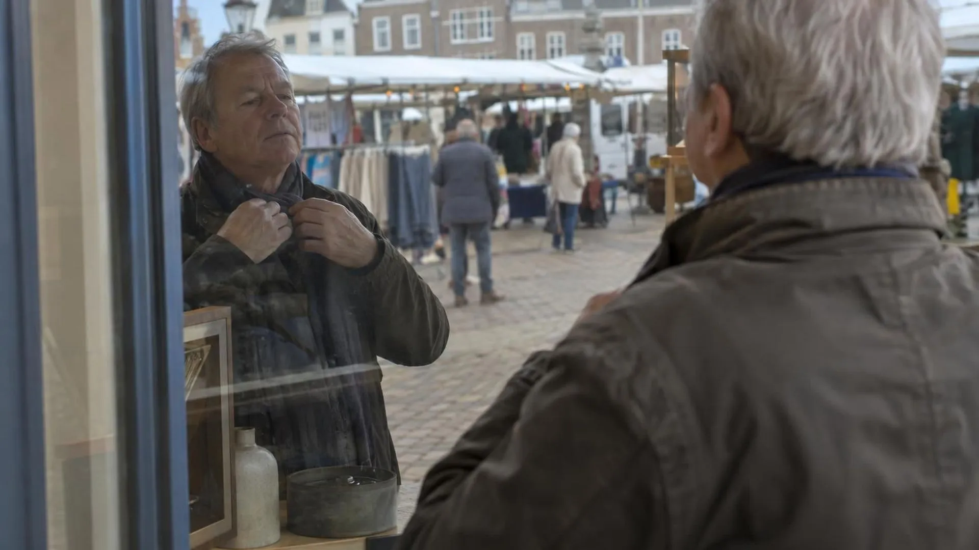 Iemand bekijkt zichzelf in de weerspiegeling van een etalageruit op een marktplein