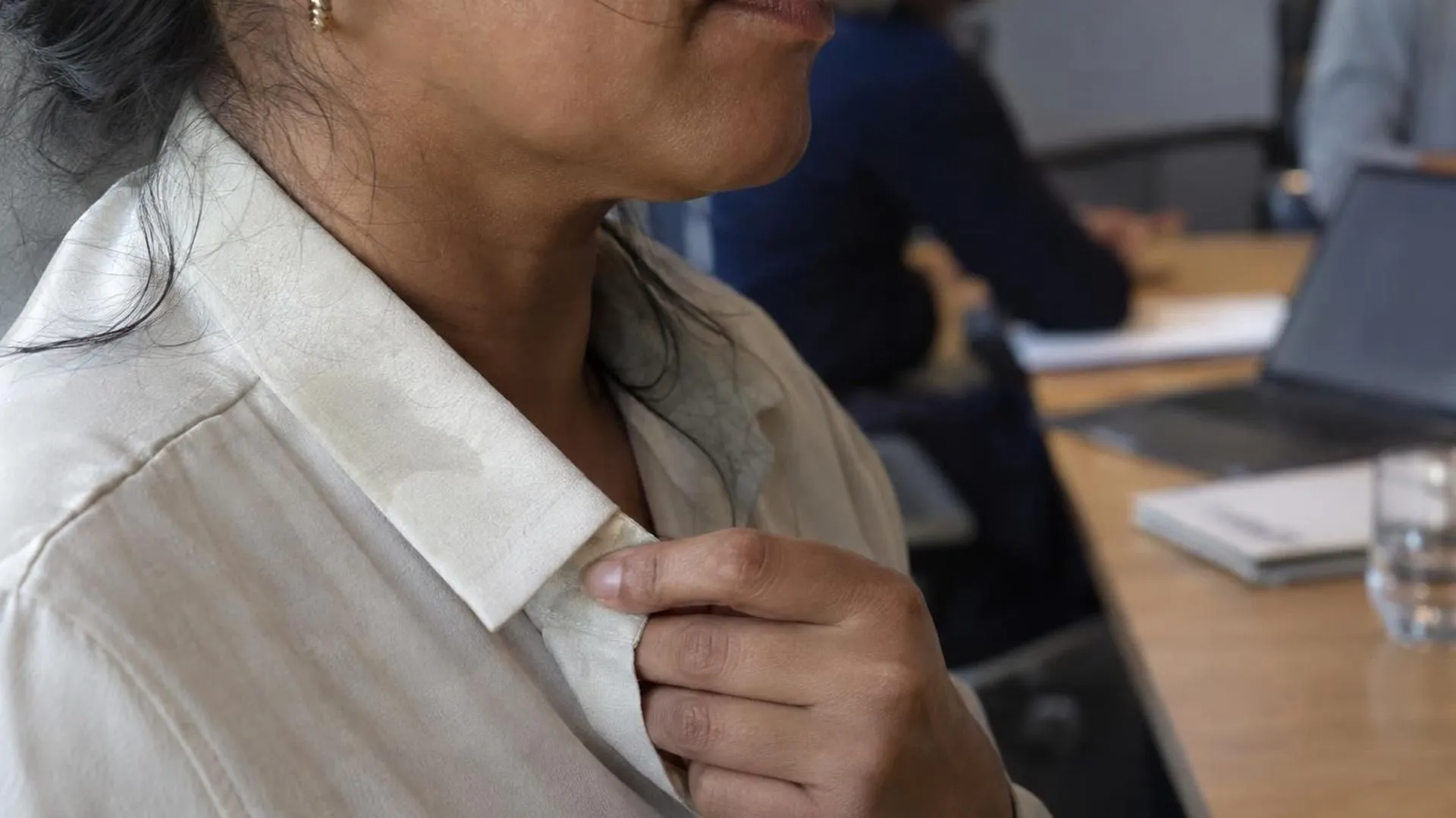 Close-up van een boordje met een vage vochtplek, een hand trekt er lichtjes aan tijdens een vergadering.