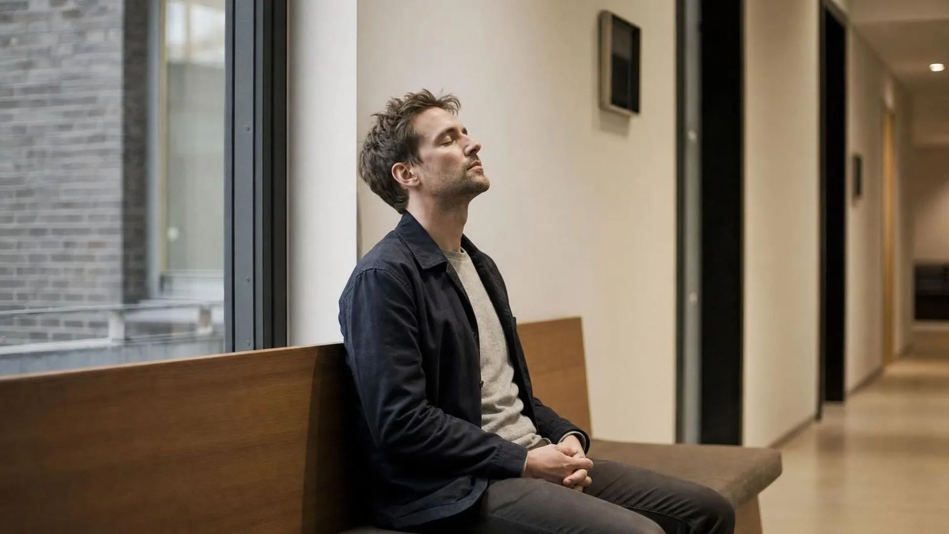 Man op een bankje in een rustige gang, ogen dicht