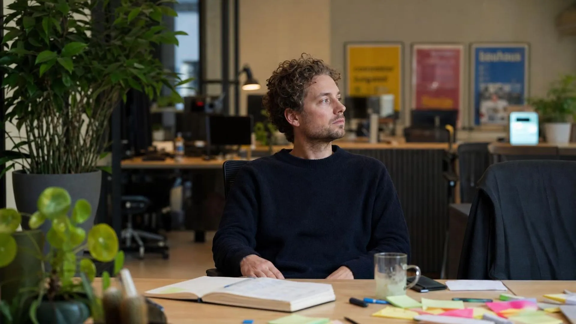 Persoon zit aan een drukke werktafel en staart voor zich uit